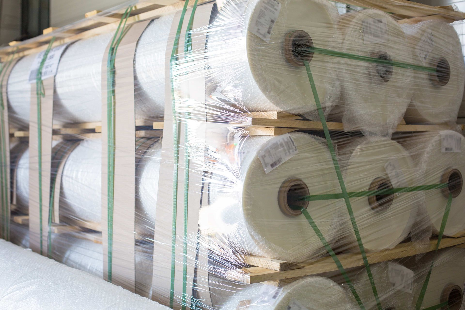 Stacked rolls of white material wrapped in plastic and strapped on a pallet