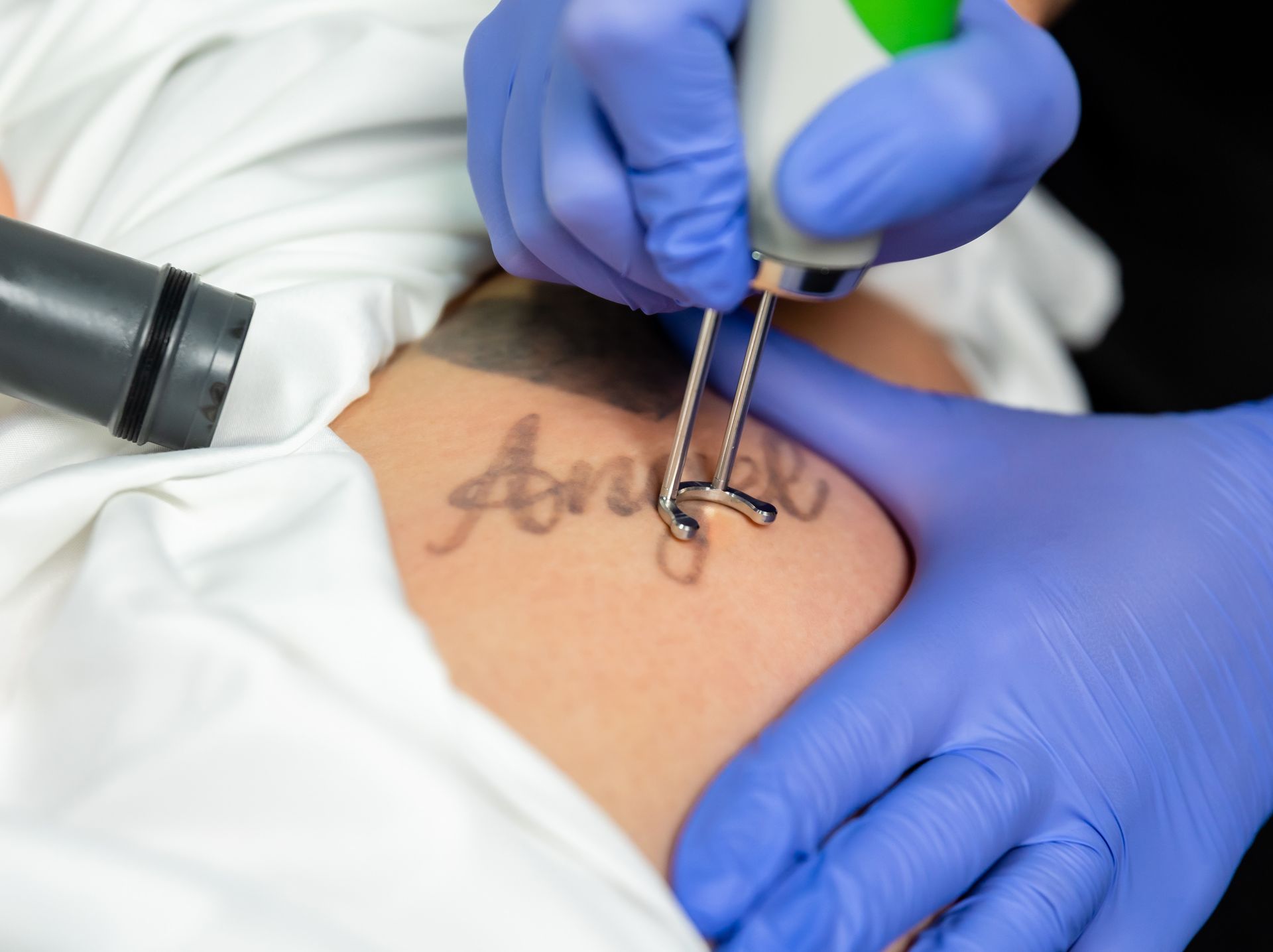 Gloved hands tattooing cursive text on a person’s forearm in a close-up shot