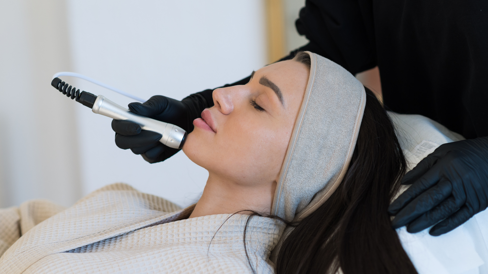 Woman receiving a facial treatment with a handheld skincare device, lying on a spa bed
