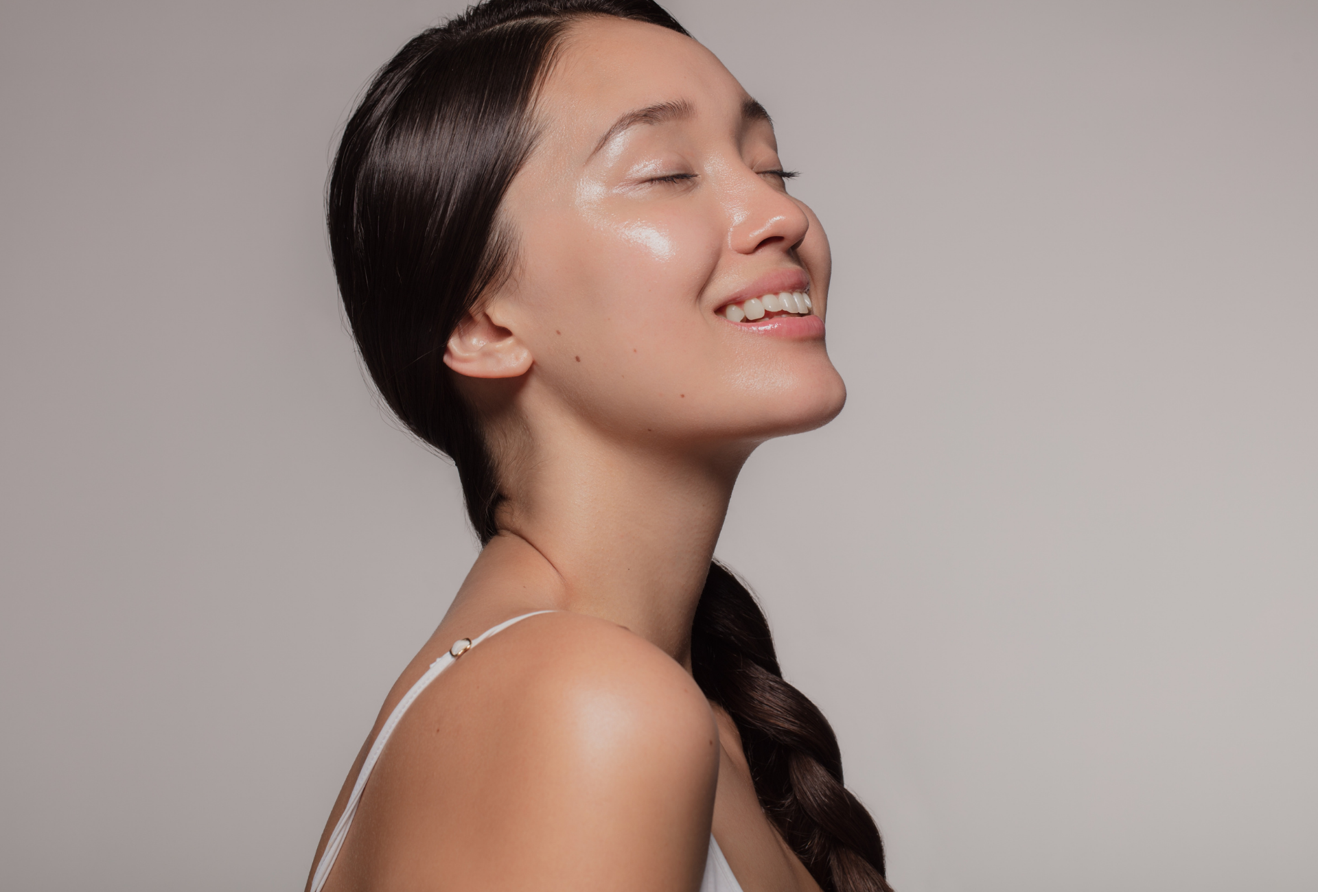 Woman with dark hair in a braid, smiling in profile against a neutral background