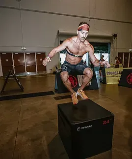Man jumping onto a black box. Indoors, Spartan Race logo visible.
