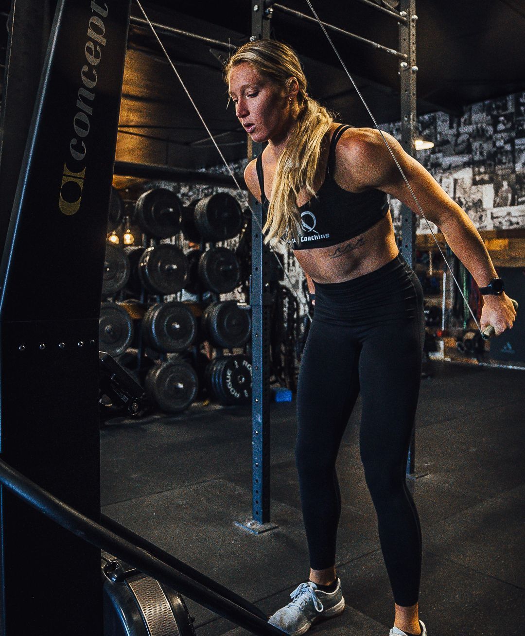 Woman in gym exercising on a cable machine, pulling cables, wearing athletic wear.