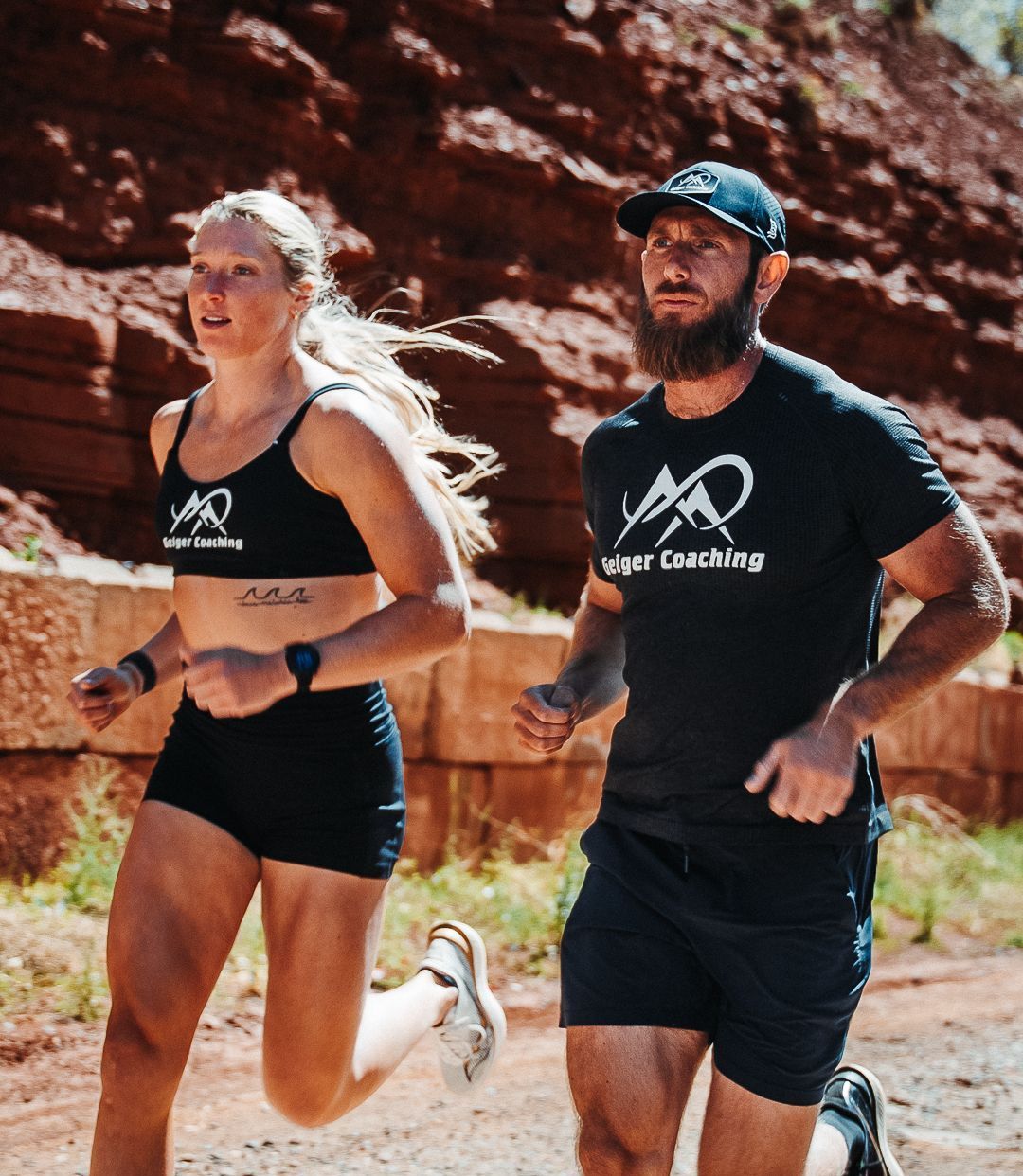 Woman and man running outdoors on a trail. Both wear athletic attire. Red rock canyon in the background.