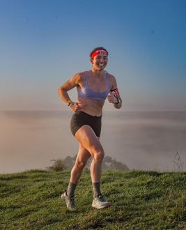 Woman running on grassy hill, wearing athletic gear, smiling. Fog in background.