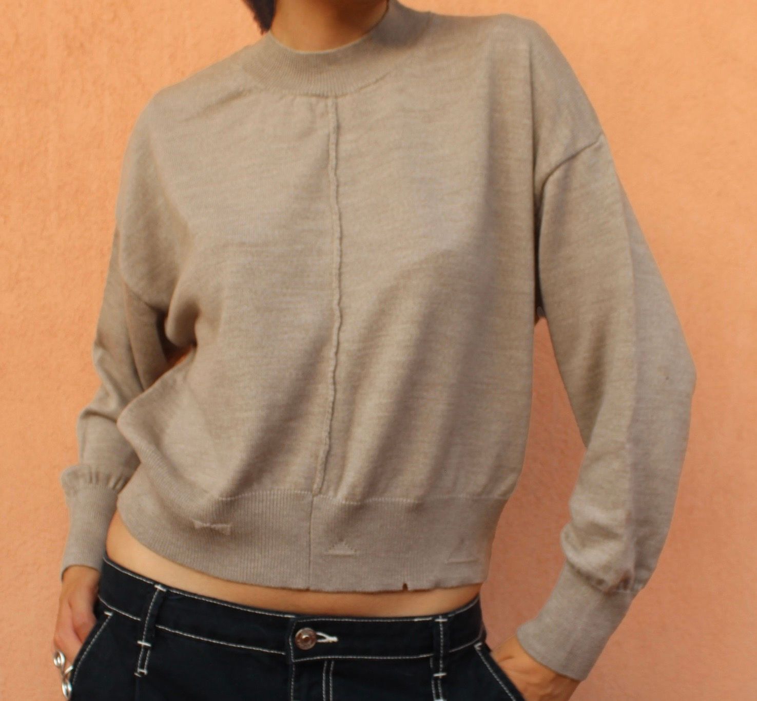 Persona che indossa un maglione dolcevita di colore chiaro e tiene le braccia incrociate.