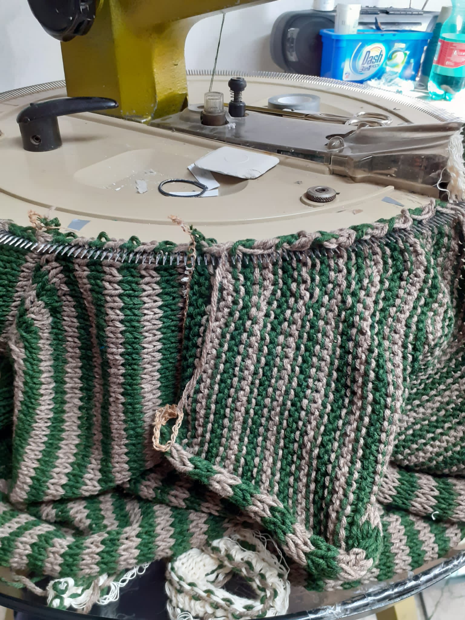 Tessuto lavorato a maglia a righe verdi e beige in lavorazione, su un tavolo rotondo con una macchina da cucire e i relativi materiali.