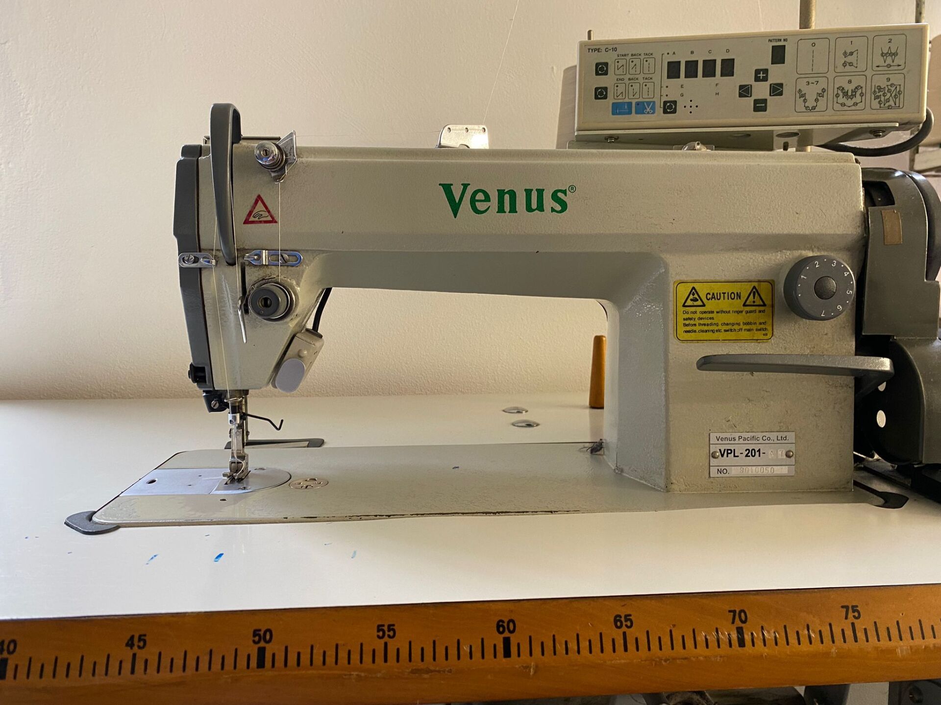 Una macchina da cucire industriale del marchio Venus su un tavolo bianco. La macchina è beige e ha un pannello di controllo sulla parte superiore.