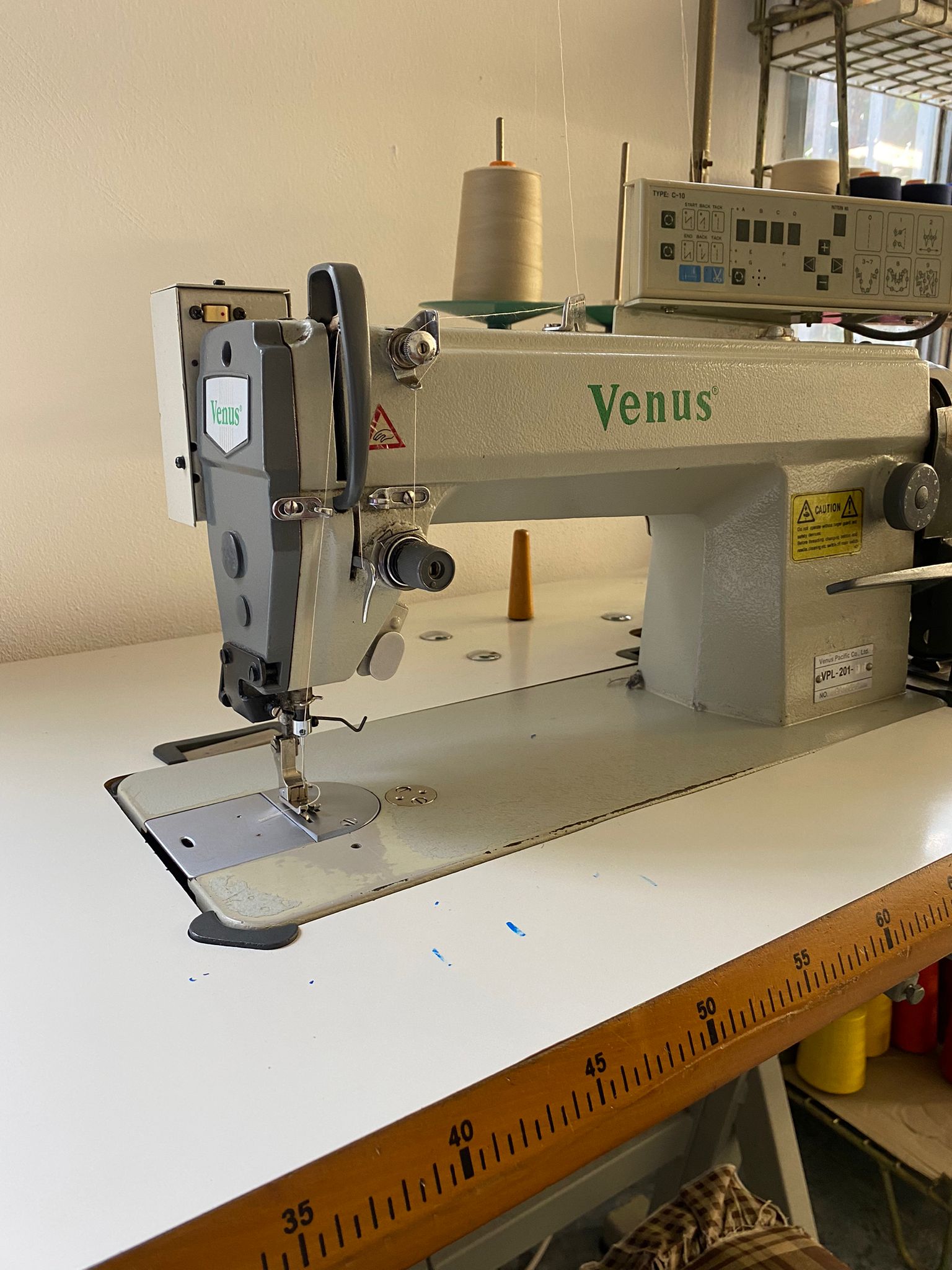 Una macchina da cucire industriale Venus su un tavolo bianco. Beige e grigio, con rocchetto di filo e ago visibili.