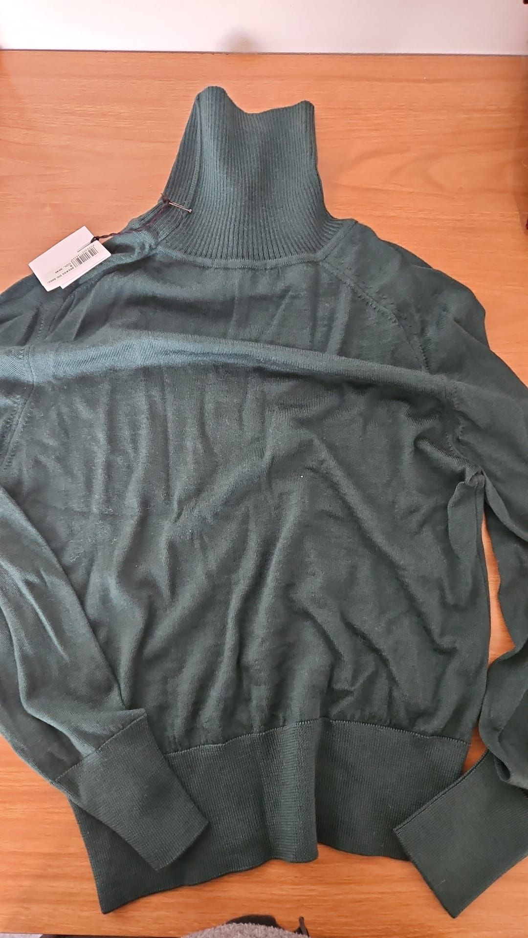 Maglione verde a collo alto con un'etichetta con il prezzo su una superficie di legno.