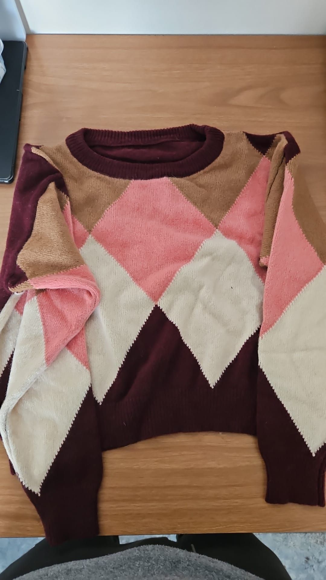 Maglione con motivo a rombi nei colori bordeaux, rosa, beige e crema su una superficie di legno.