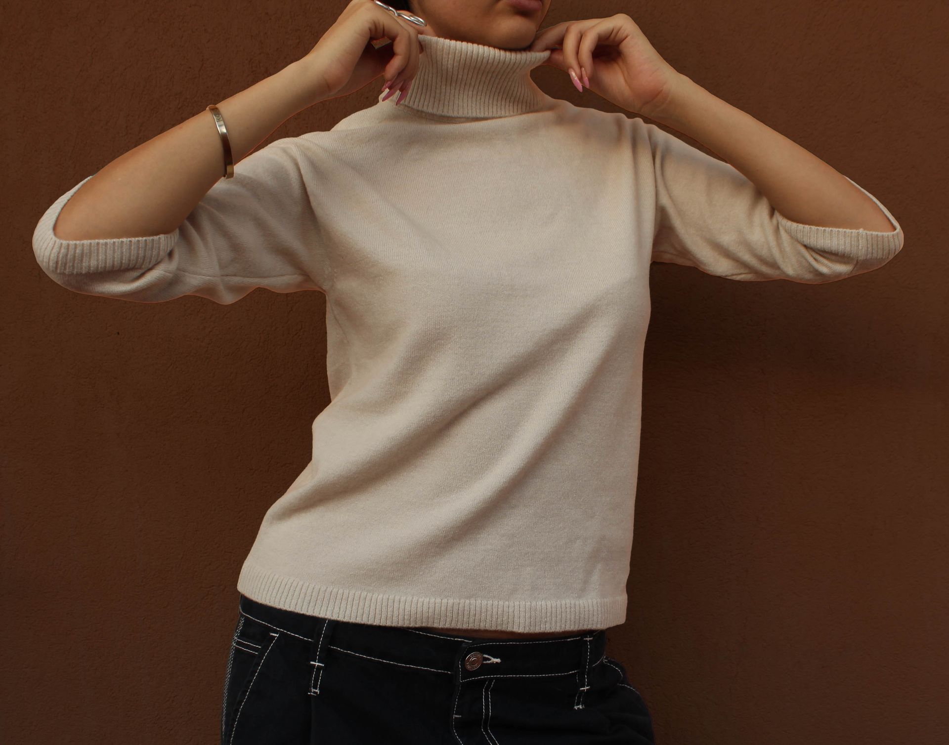 Persona che indossa un maglione dolcevita di colore chiaro e tiene le braccia incrociate.