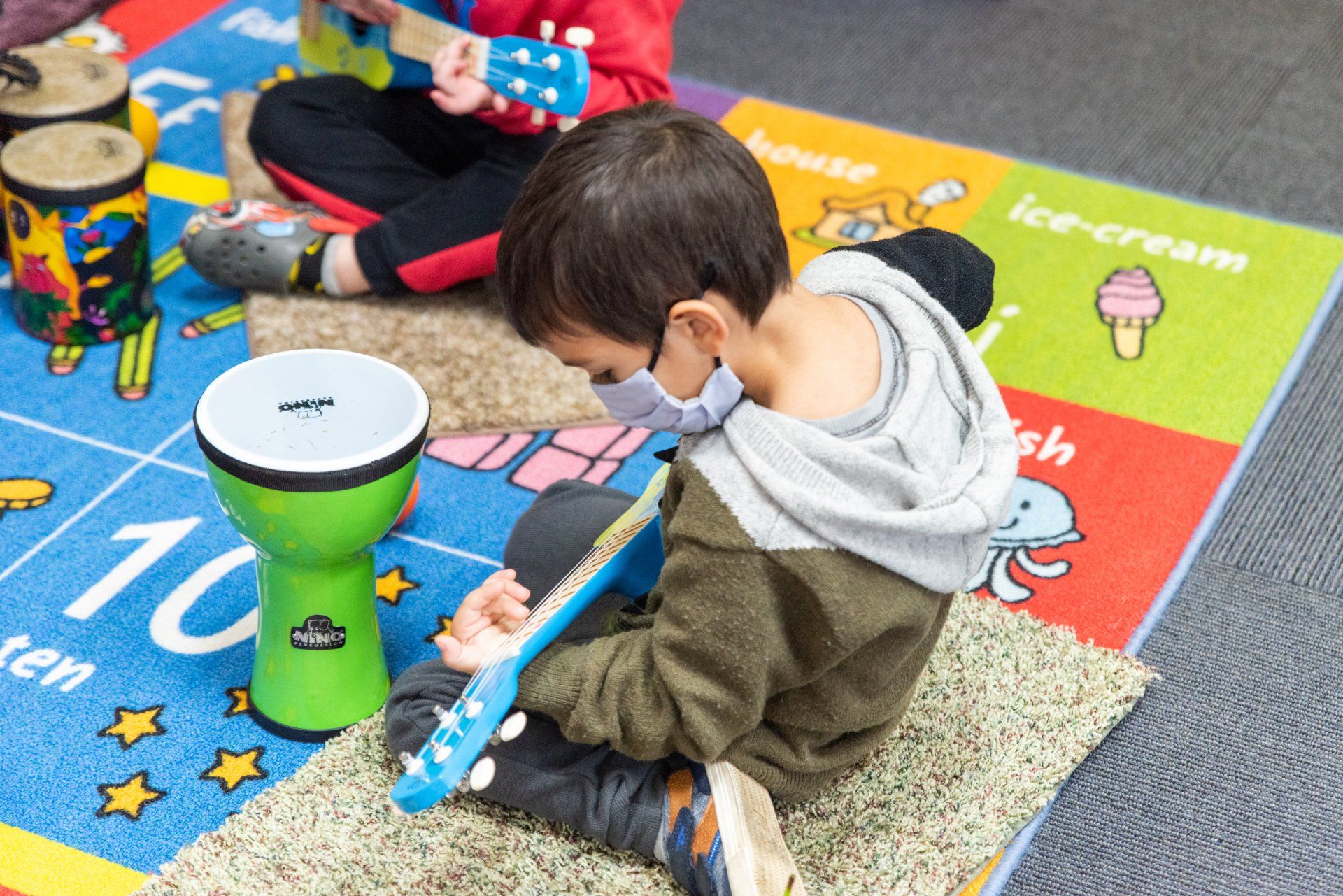 little boy playing guiltar on the carpet at school