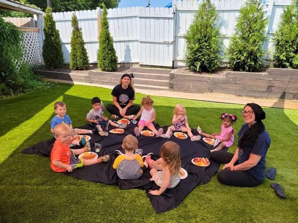 teachers with preschool students eating on a blanket outside