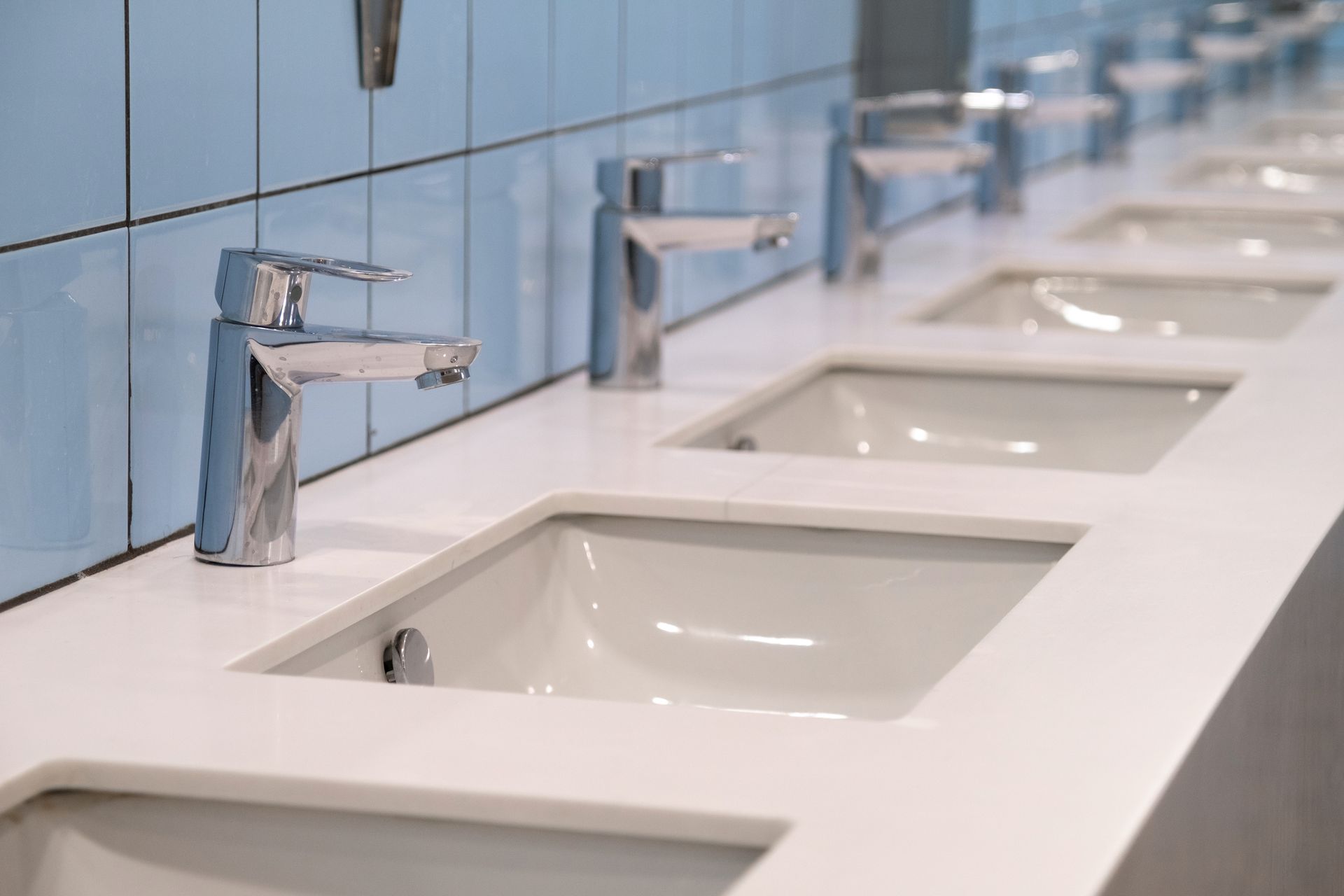 A row of white sinks in a public restroom with blue tiles.