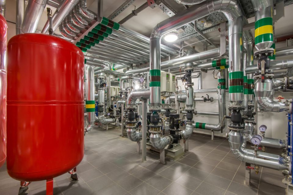 Industrial plant machinery with silver pipes and valves beside a large red tank in a clean utility room