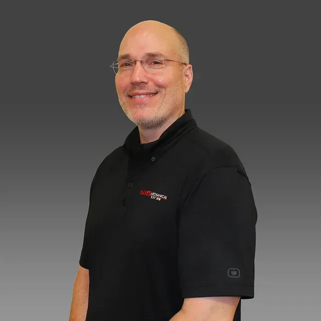 Smiling bald man in black polo shirt standing against a gray background