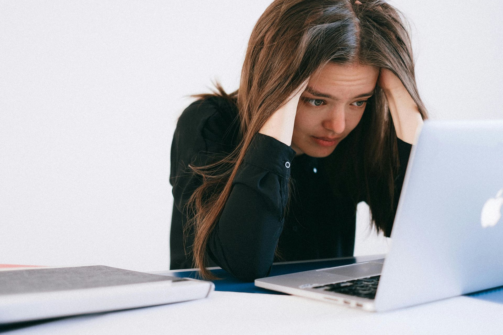 Woman with hands on head looking distressed at laptop on a desk.