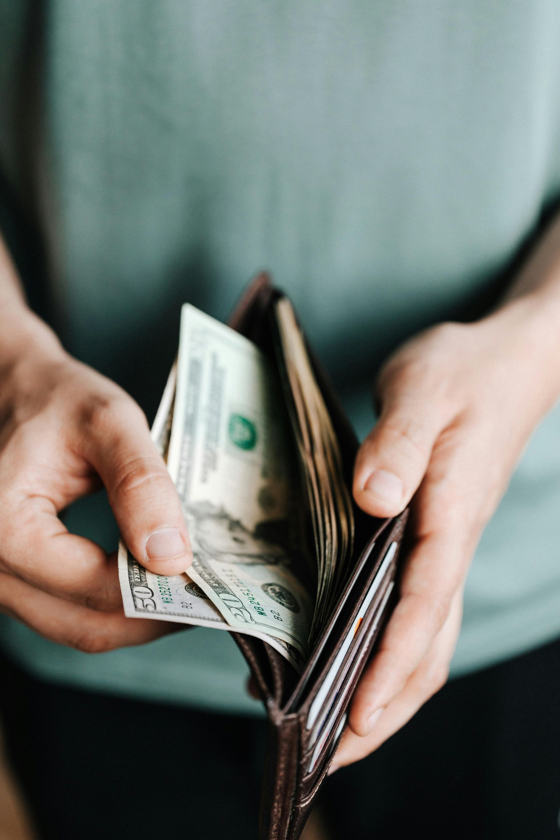 Person holding a brown wallet with several US dollar bills visible.