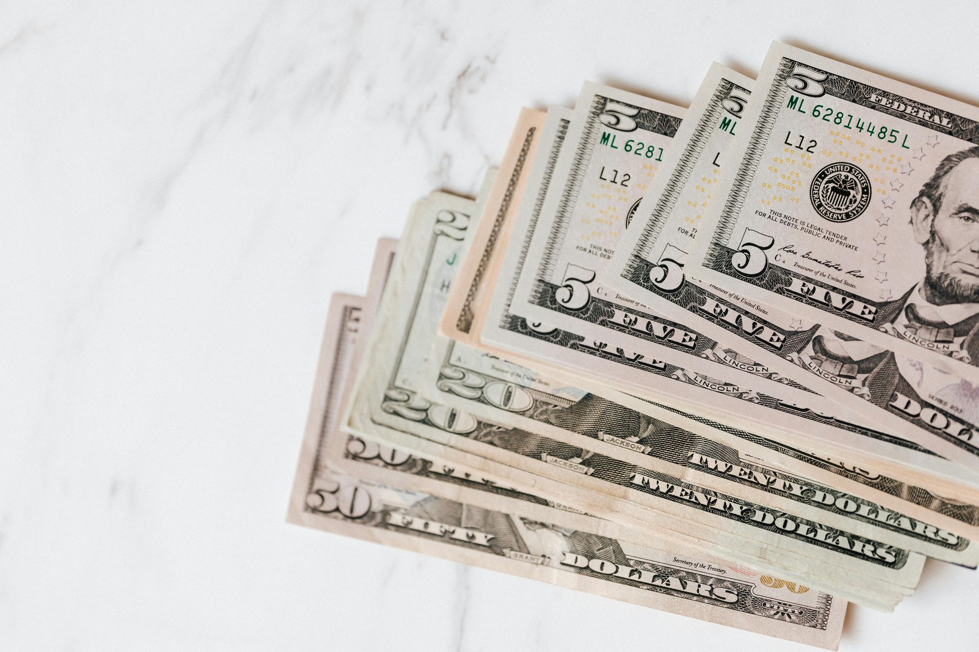 Cash, including five and fifty-dollar bills, fanned out on a white marble surface.