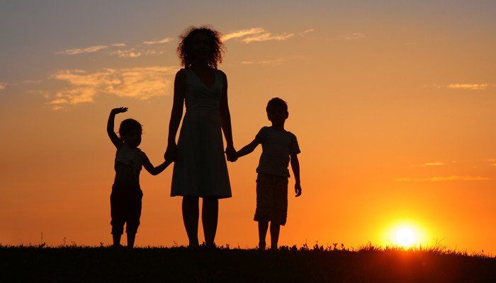 A woman holding hands with two young boys and watching a sunset