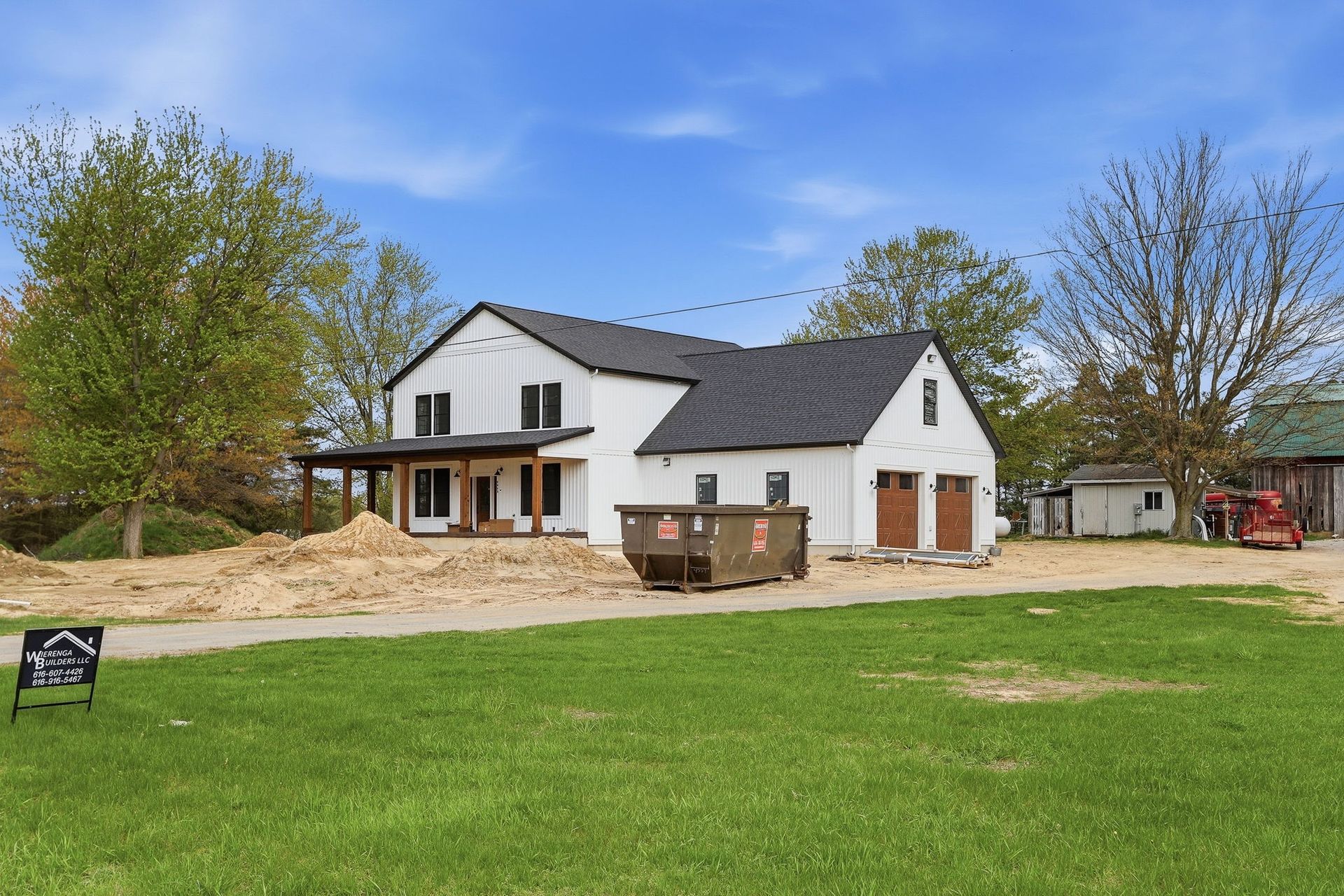 White two-story house with black roof, front porch, and green lawn under cloudy sky