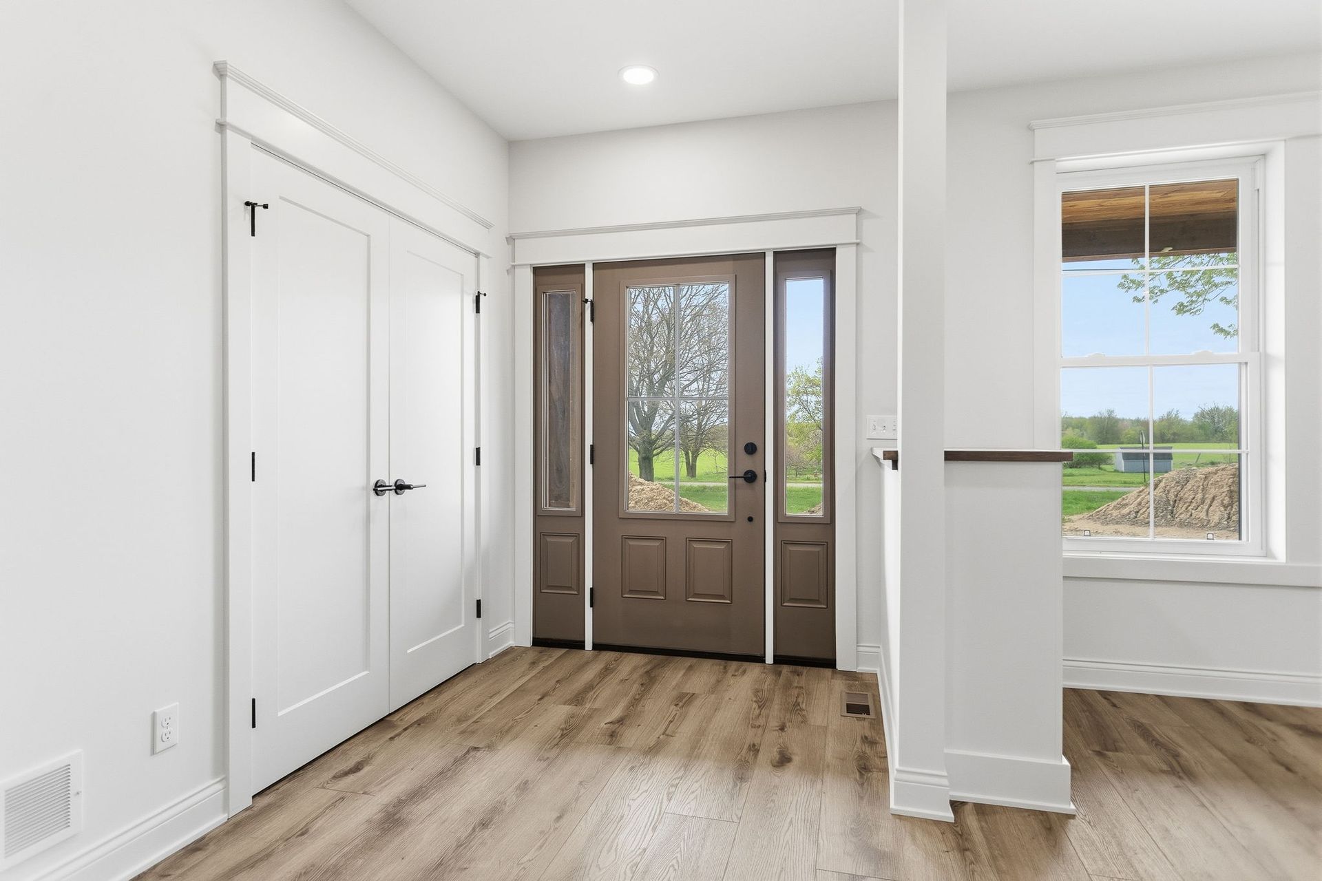 Bright entryway with a brown front door, white walls, closet doors, and a windowed side wall