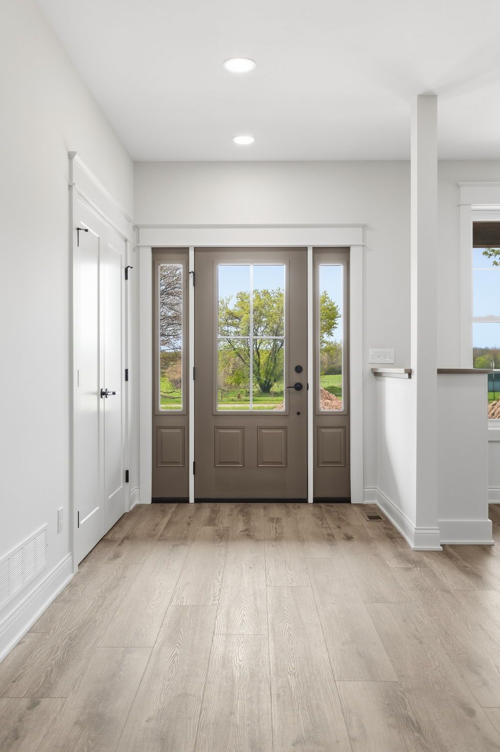 Bright entry hallway with white walls, wood floors, and a front door with glass sidelights.