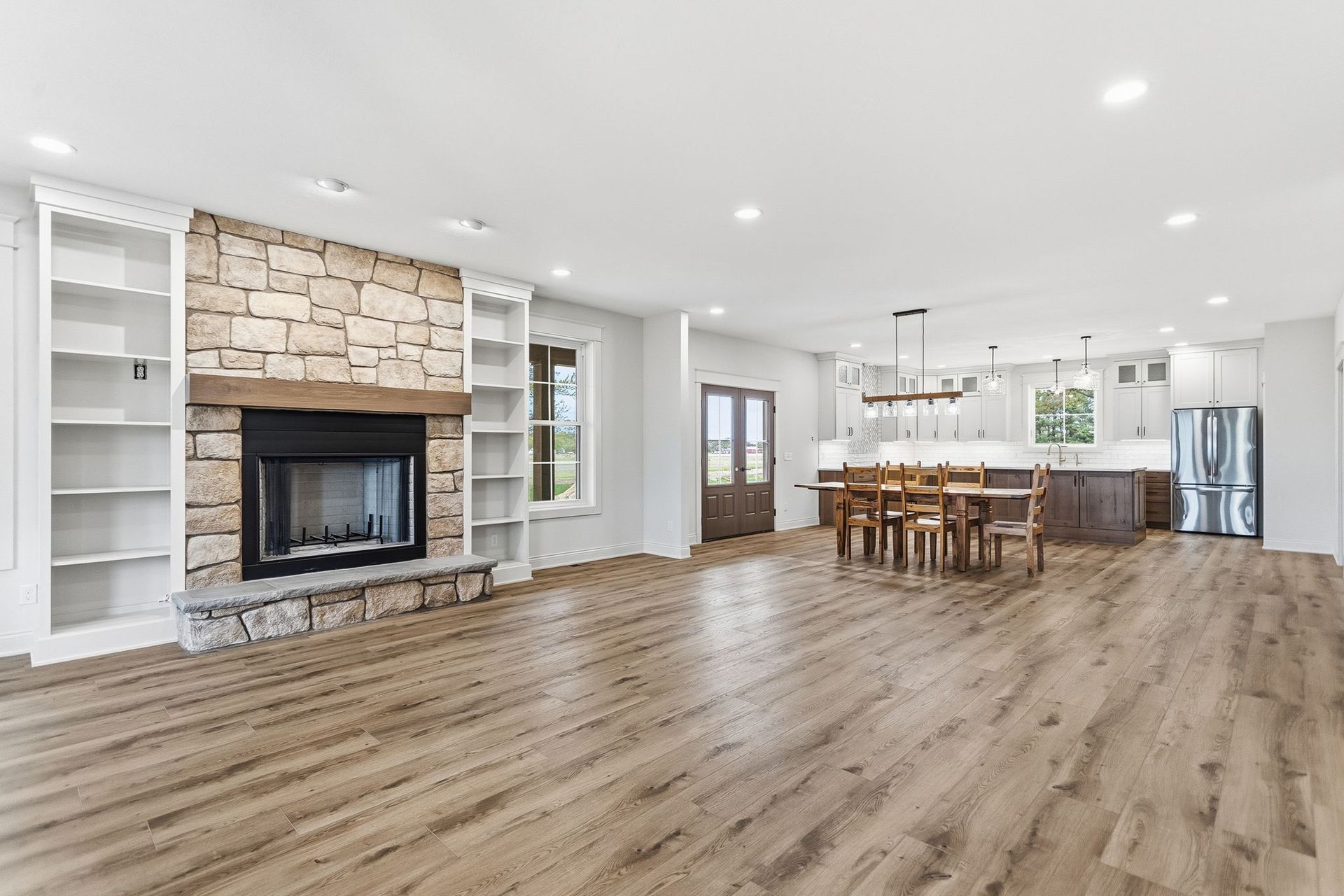 Bright open-concept living room with stone fireplace, wood floors, and kitchen island