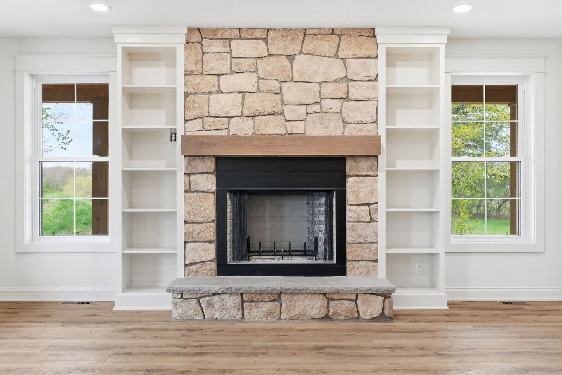 Stone fireplace with built-in white shelves and windows in a bright living room