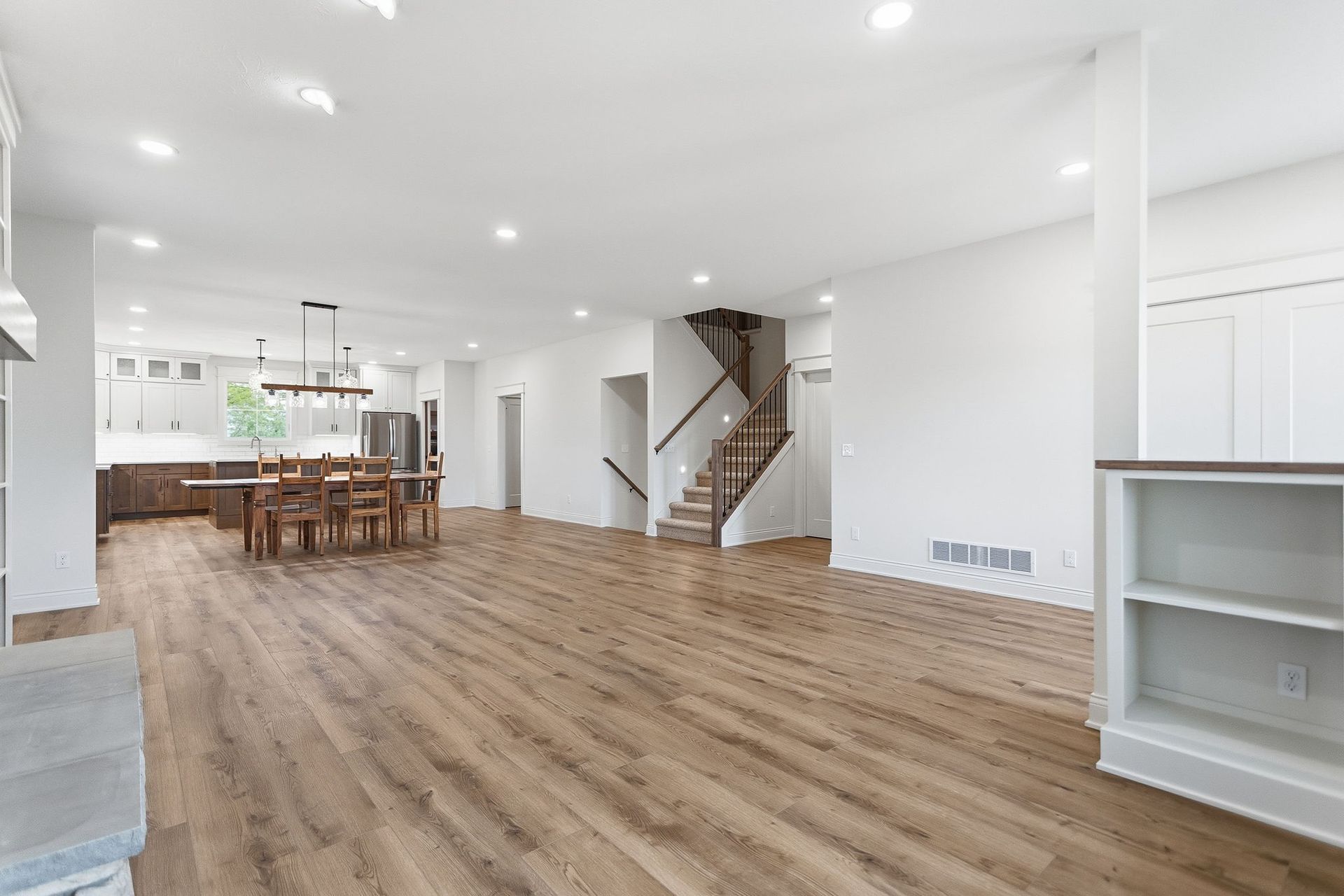 Bright open-plan living room with wood floors, staircase, and kitchen island in the background