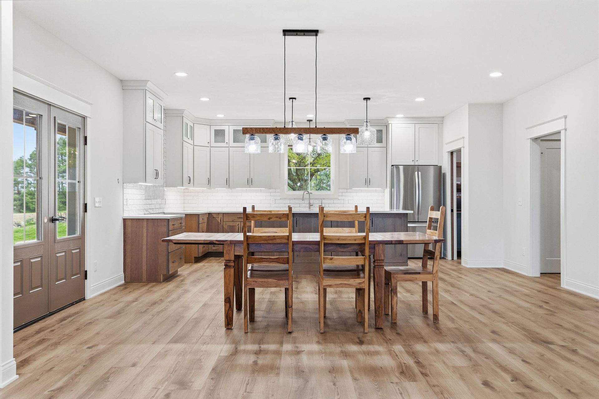 Bright modern kitchen and dining area with white cabinets, wood floors, and a wooden table with chairs