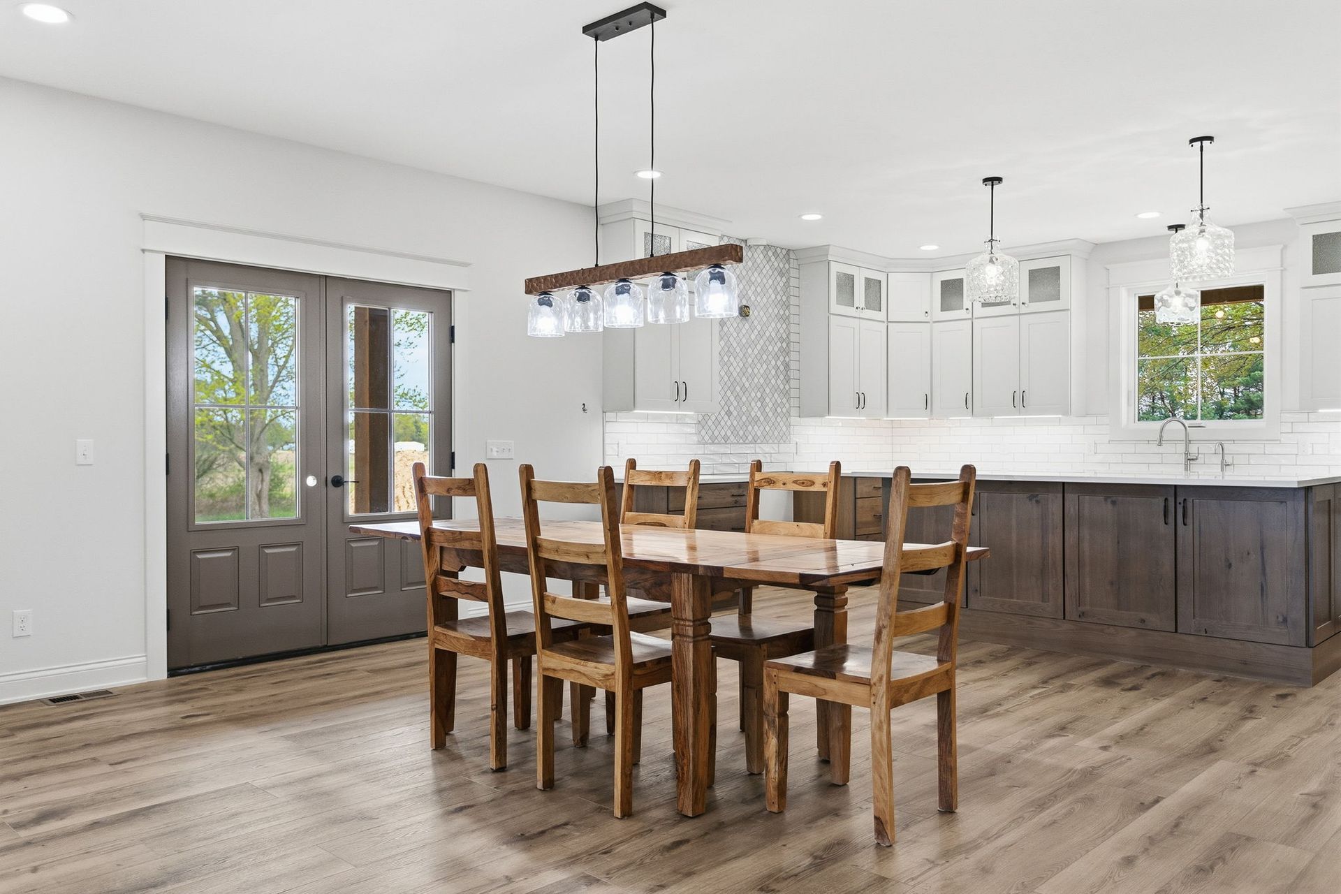 Bright modern kitchen and dining area with wooden table, chairs, white cabinets, and gray island