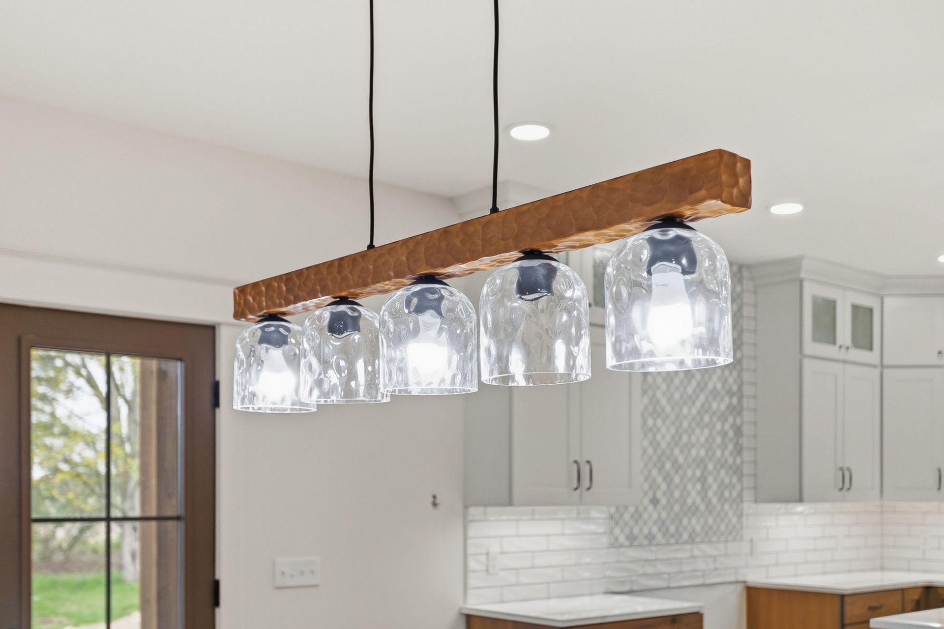 Rustic wood pendant light with five clear glass shades over a modern kitchen island