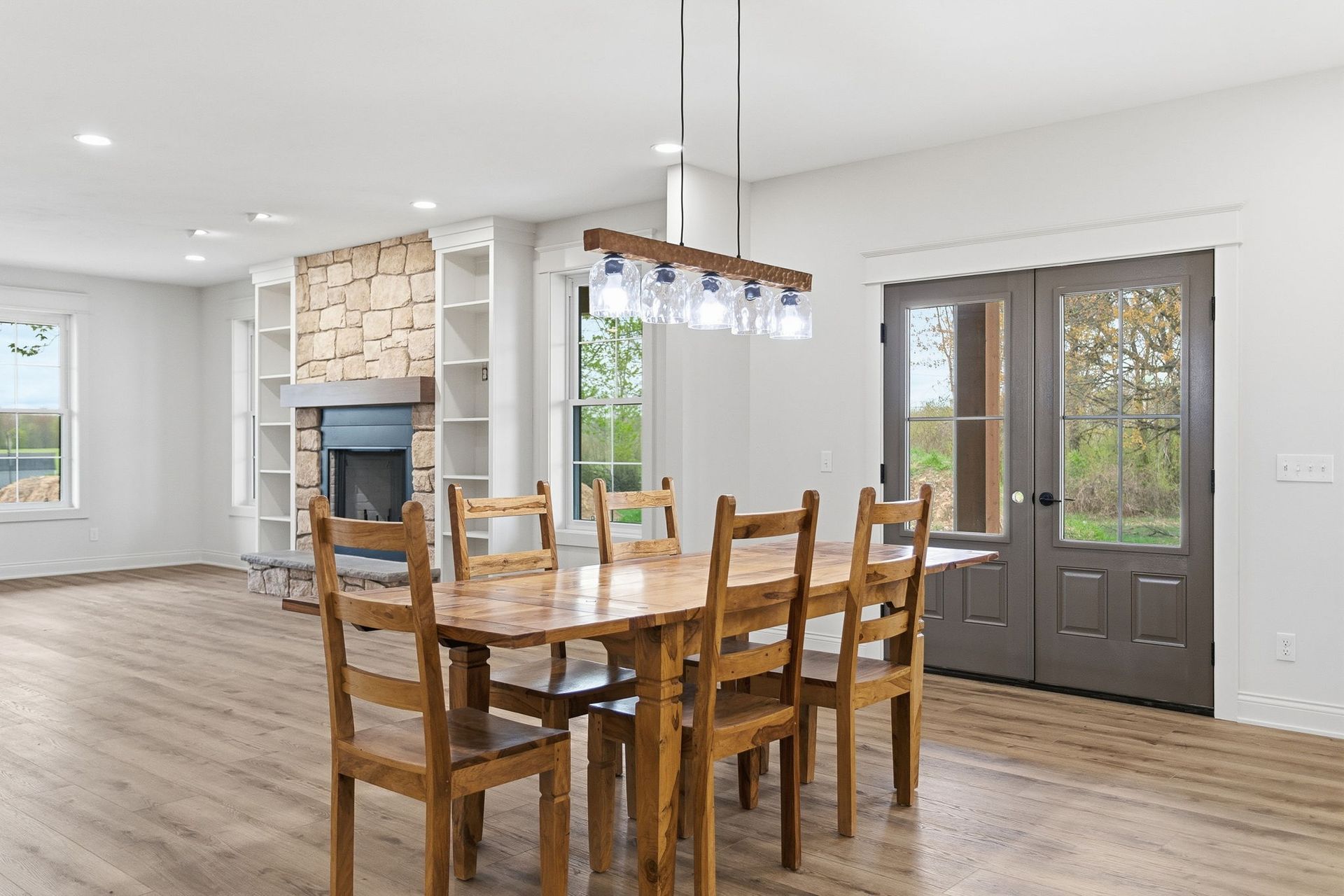 Bright dining area with wooden table, chairs, chandelier, and gray front door beside a stone fireplace.
