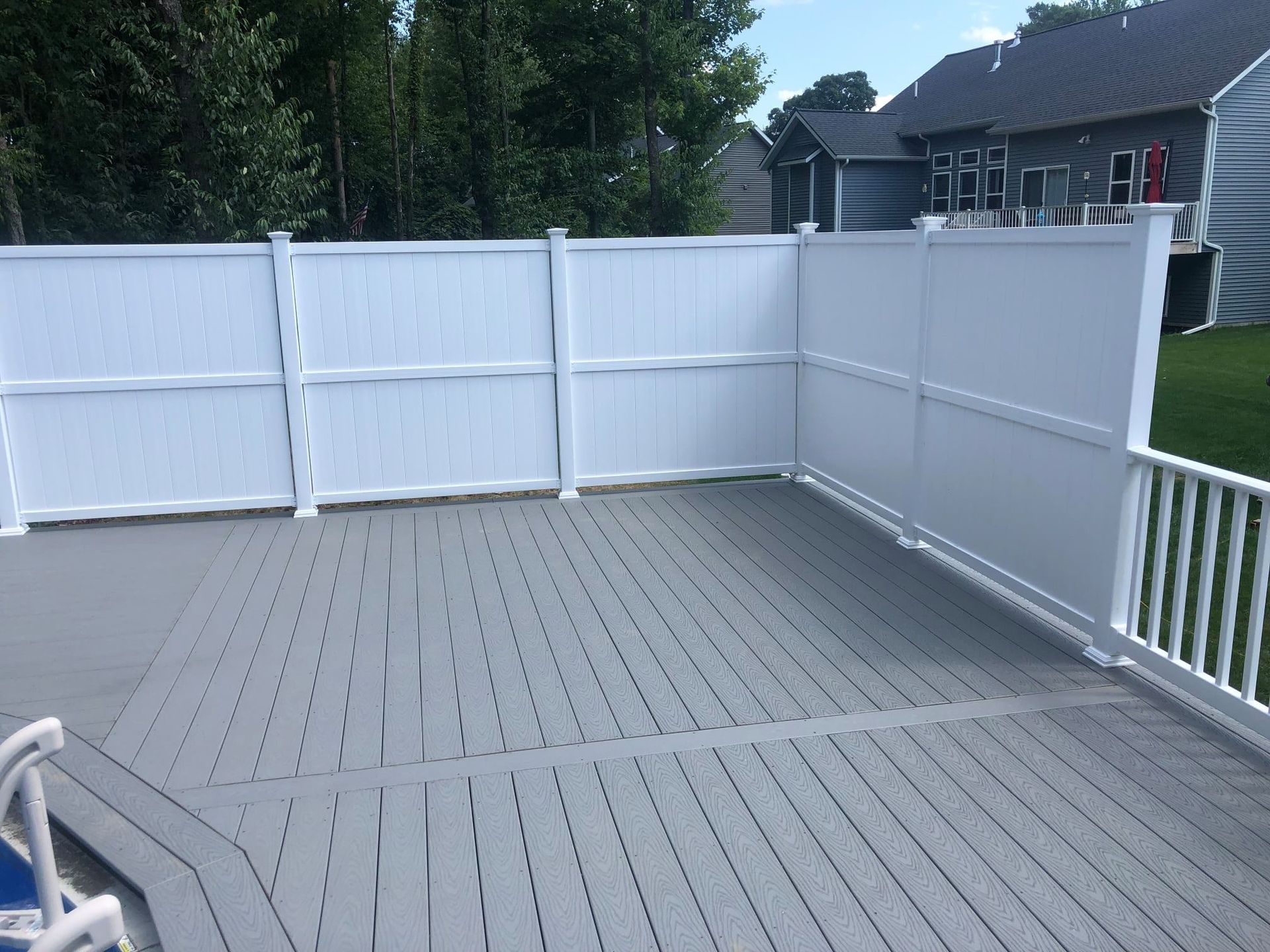 A grey composite deck features a white privacy fence cornering two sides, with a white railing on the right.