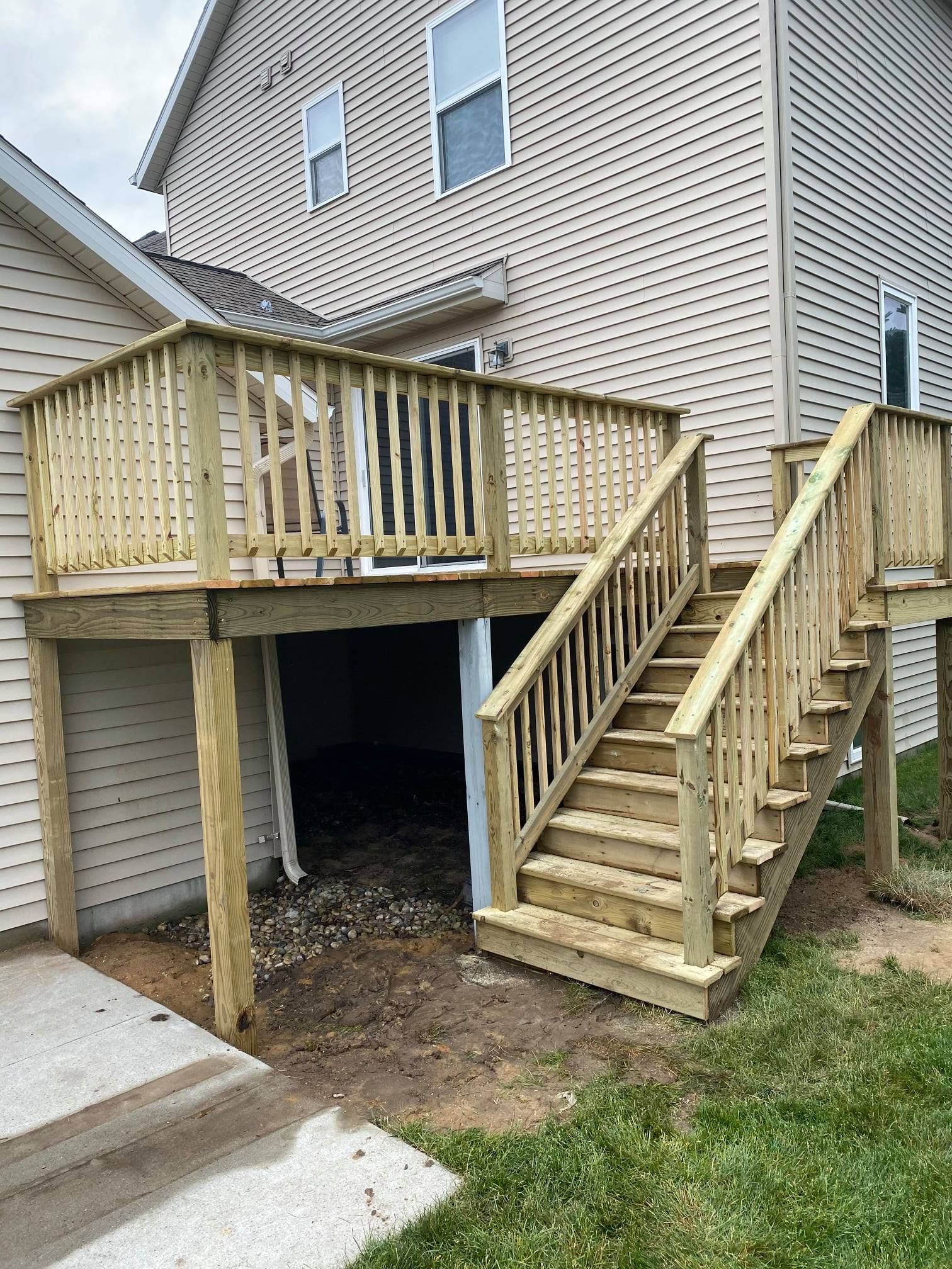 A new wooden deck with railings and stairs attached to the back of a light-colored vinyl-sided house.