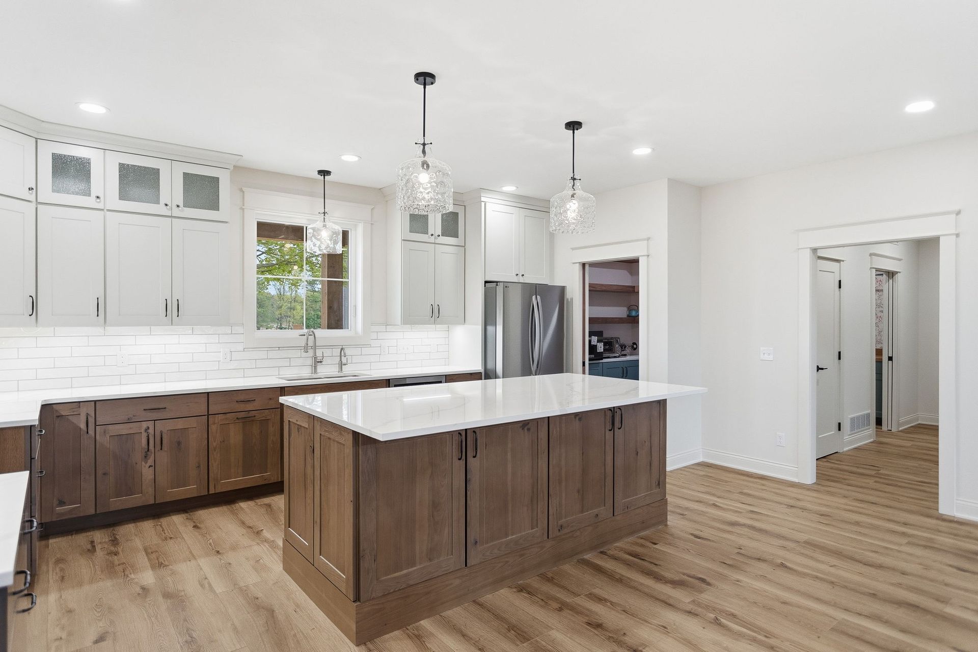 Bright modern kitchen with white cabinets, wood island, stainless fridge, and light wood floors.