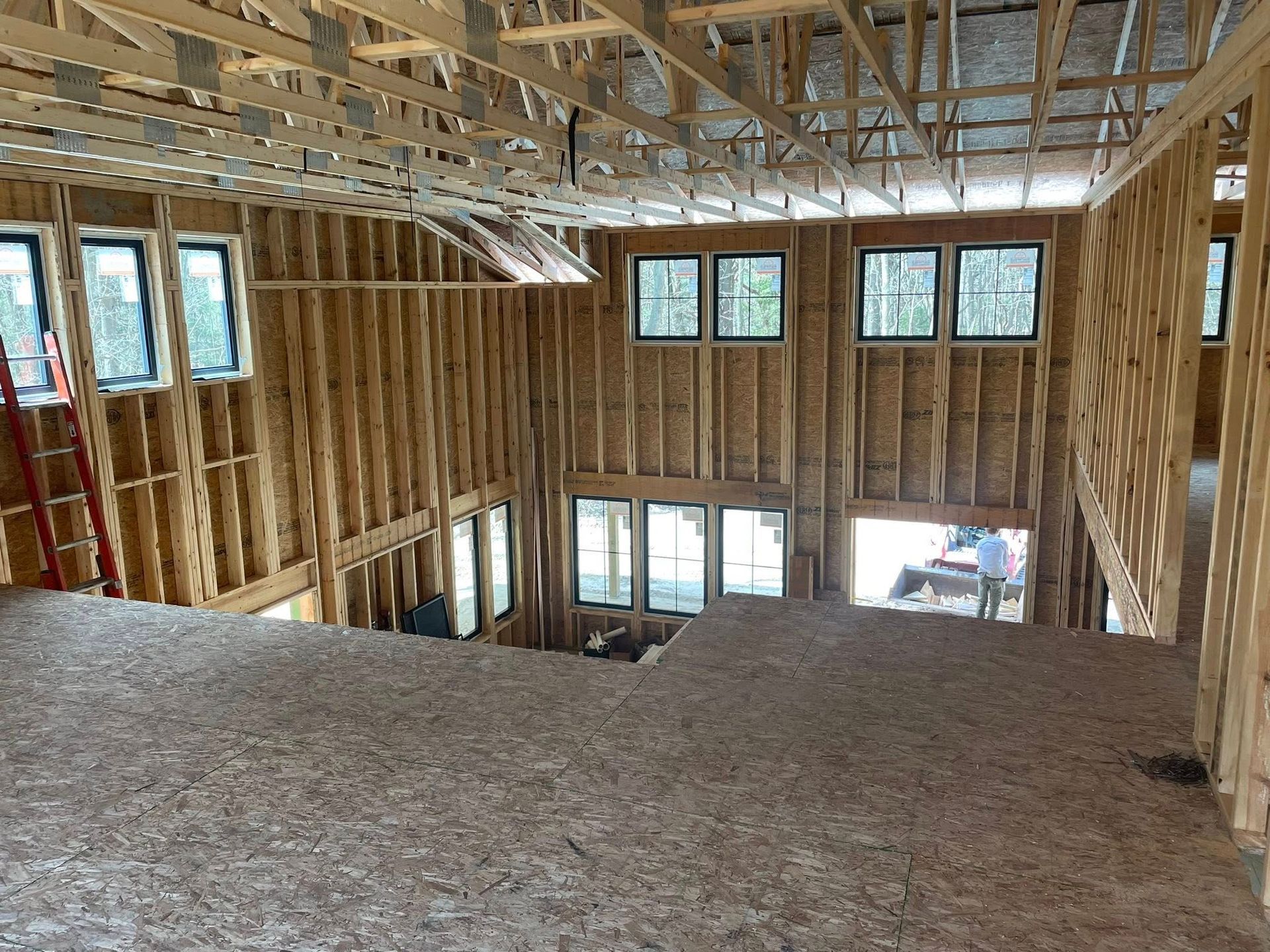 Unfinished interior of a multi-story home under construction, showing wooden wall studs, floor joists, and open windows.