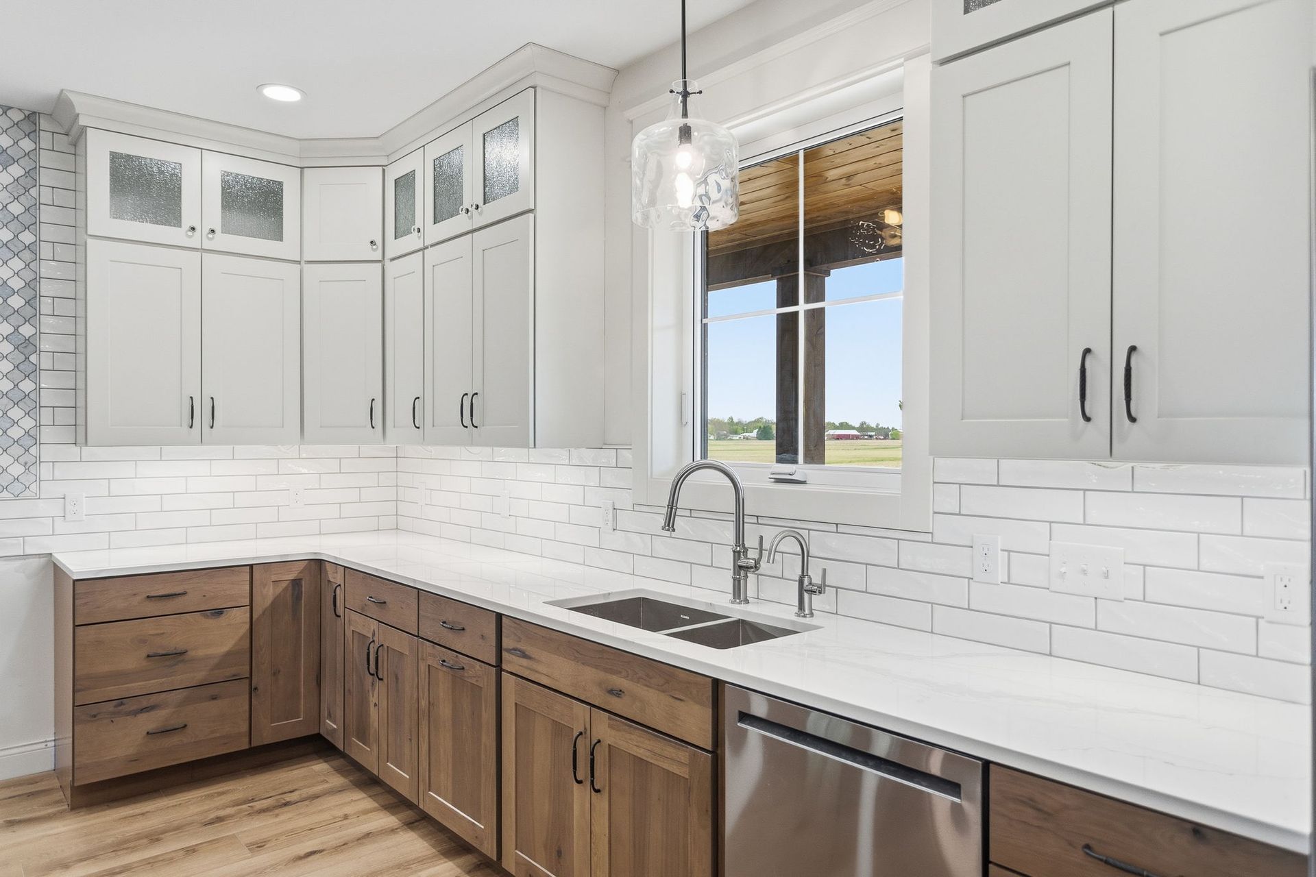 Modern kitchen with white and wood cabinets, marble backsplash, stainless dishwasher, and a window over the sink