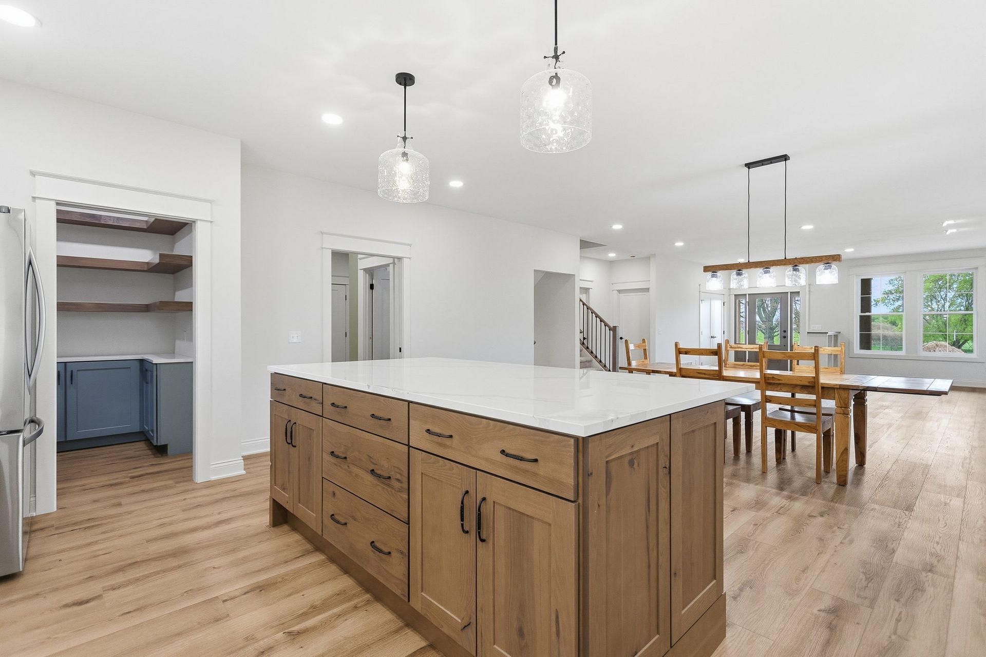 Bright open kitchen with large wooden island, light wood floors, and dining area in the background