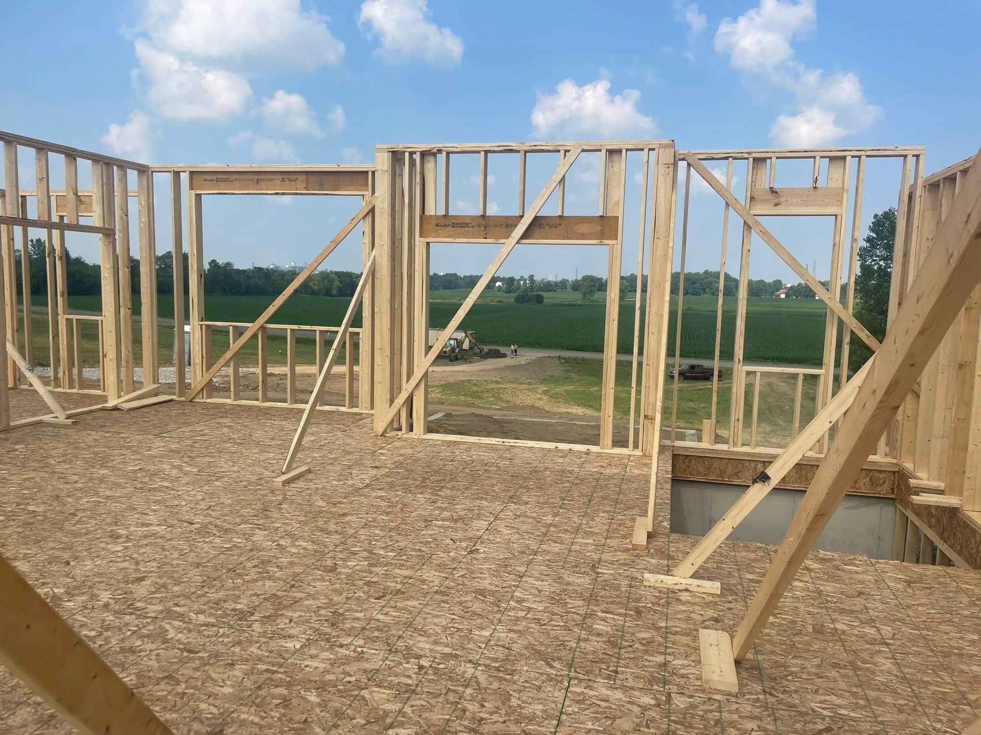Wooden framing for a house under construction, featuring open walls and structural supports overlooking a field.