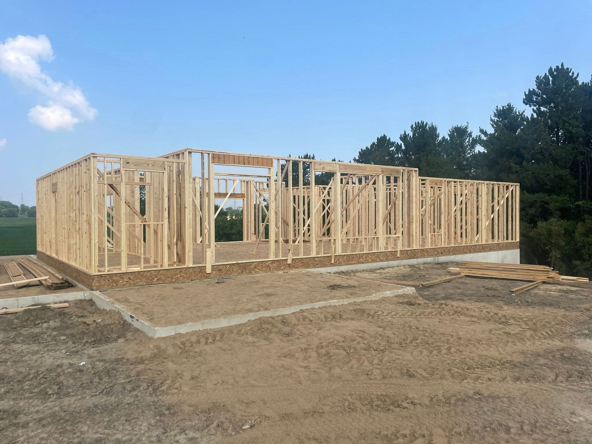 A wooden frame of a house under construction on a concrete foundation against a clear blue sky.