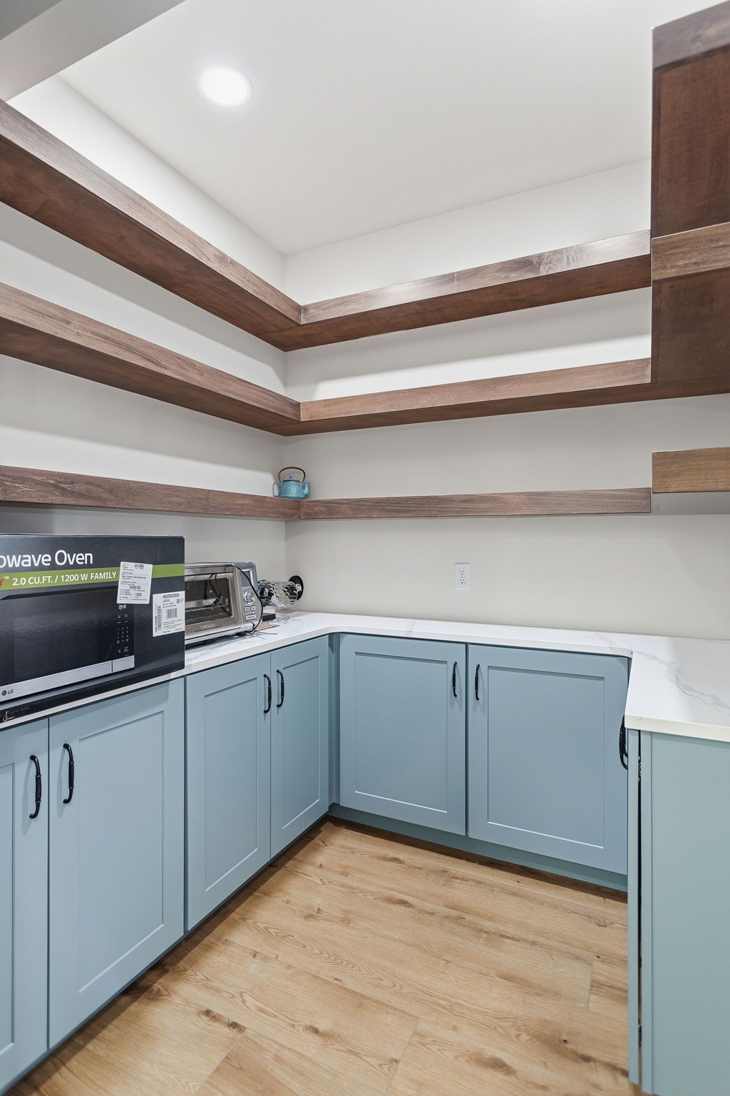 Small kitchen with light blue cabinets, white countertops, wood shelves, and a wood floor.