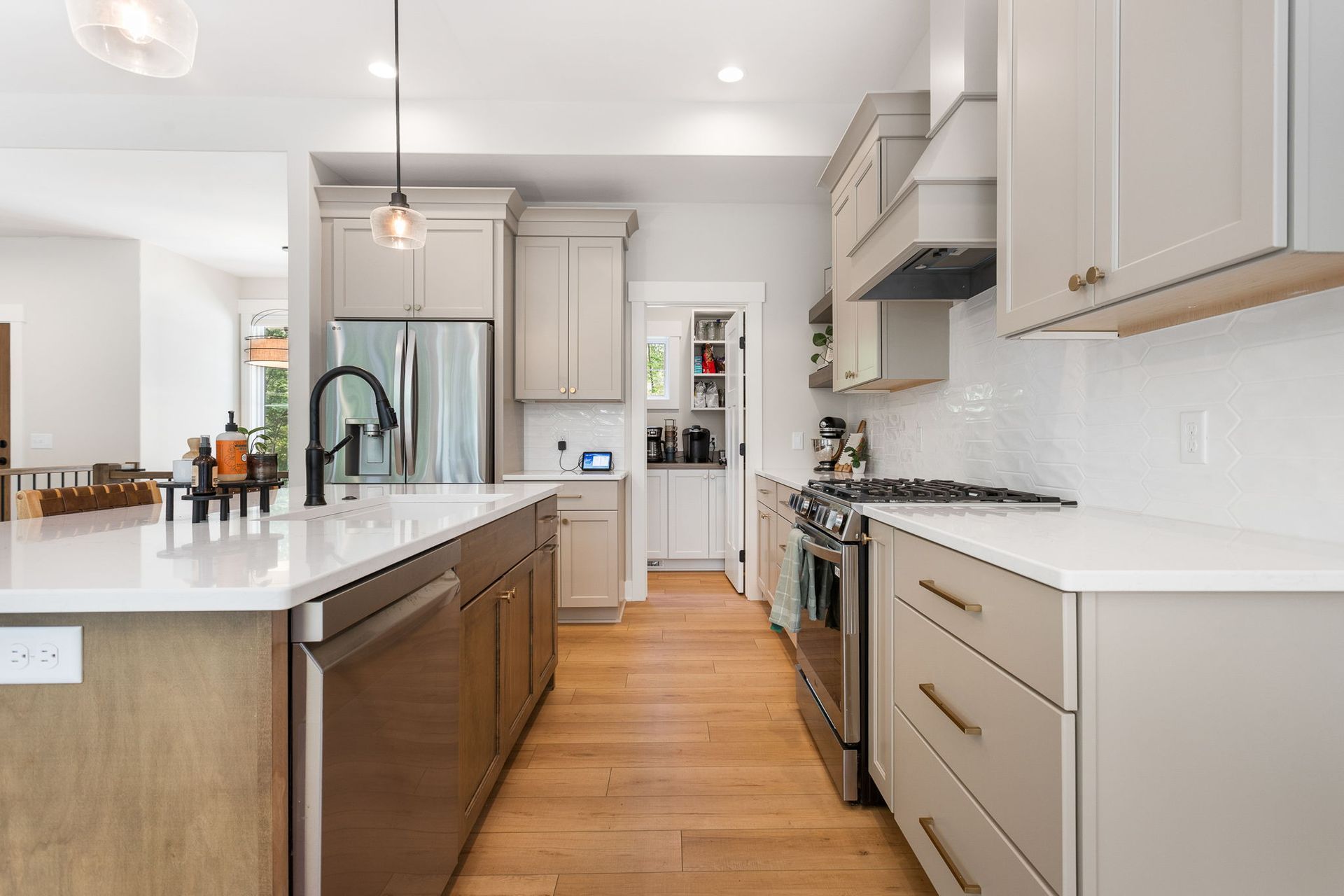 A modern kitchen with light gray cabinets, white countertops, stainless steel appliances, and wood floors.