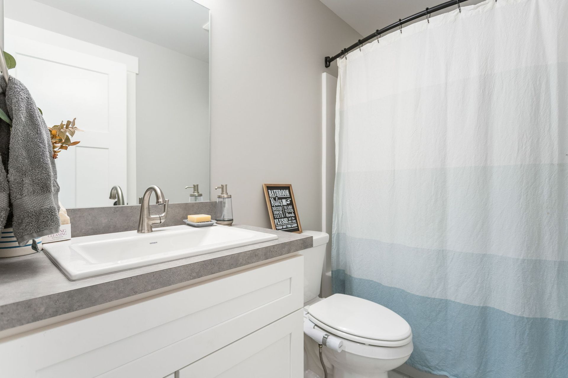 A modern bathroom with a white vanity, a concrete countertop, a sink, and a blue and white ombre shower curtain.