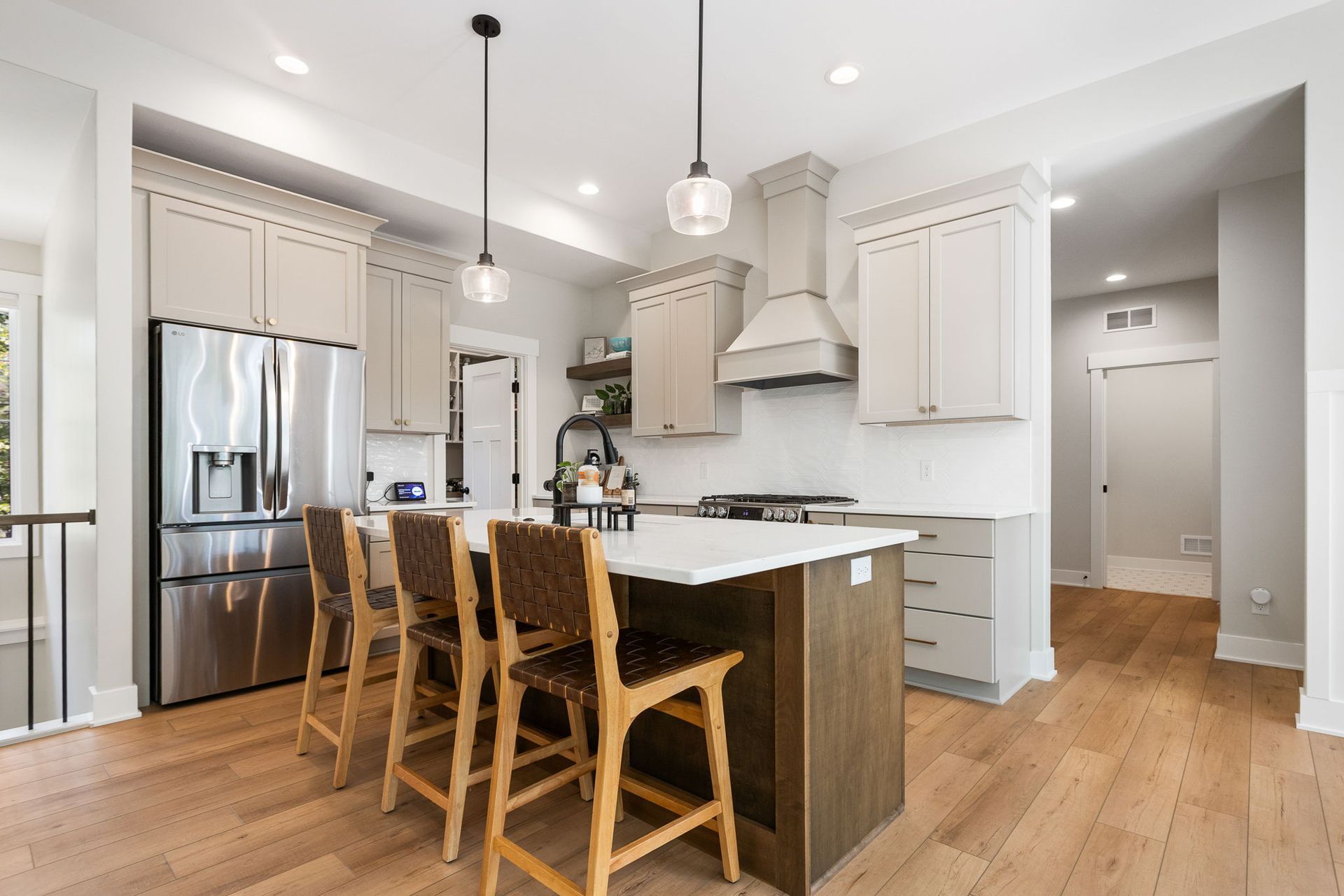 A modern kitchen with light cabinets, a wood-toned island with three stools, stainless appliances, and light wood floors.