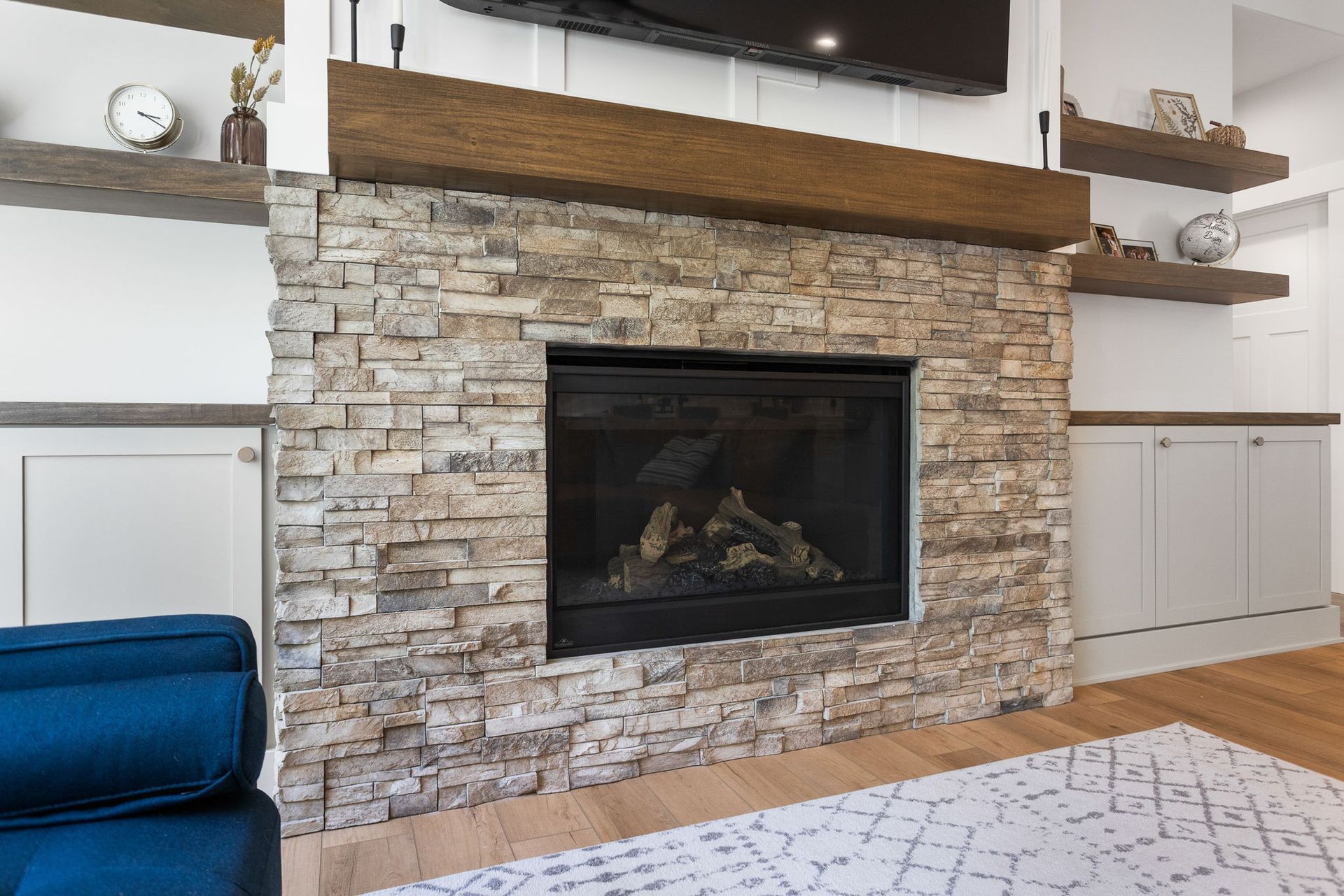 A fireplace with a stacked stone facade and a wood mantel, flanked by built-in shelves and cabinets in a living room.