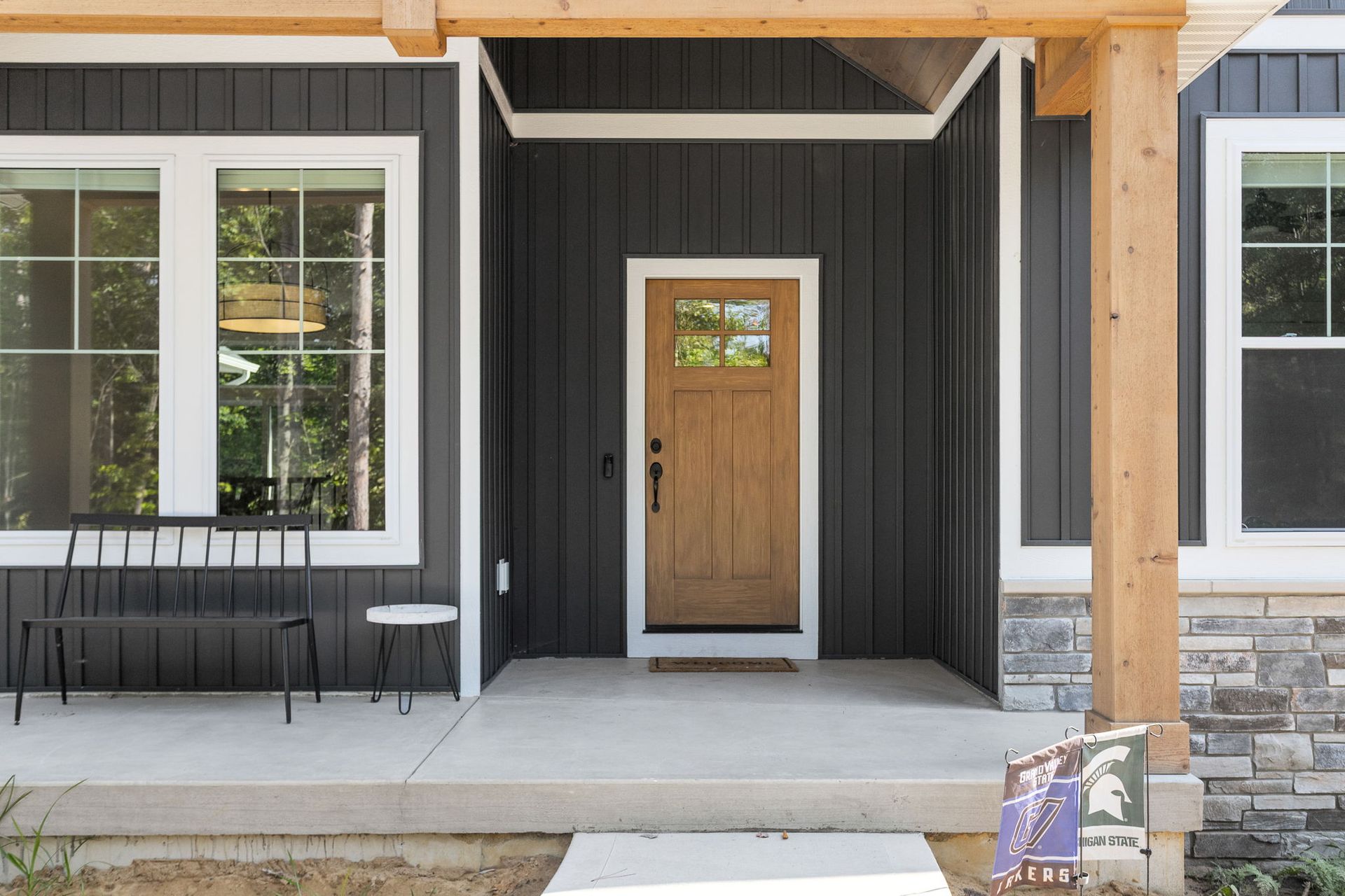 A modern front porch with dark vertical siding, a wooden front door, a black metal bench, and stone accents.