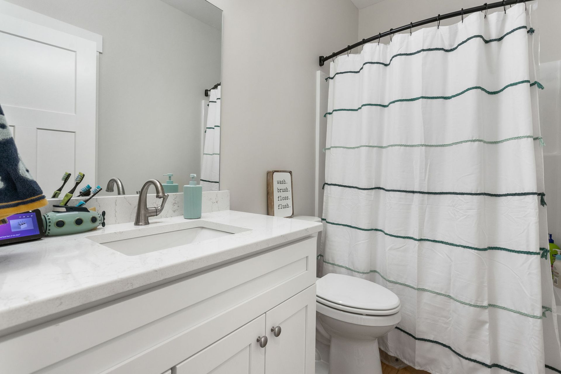 A clean, bright bathroom with a white vanity, marble-style countertop, and a shower with a white and green striped curtain.