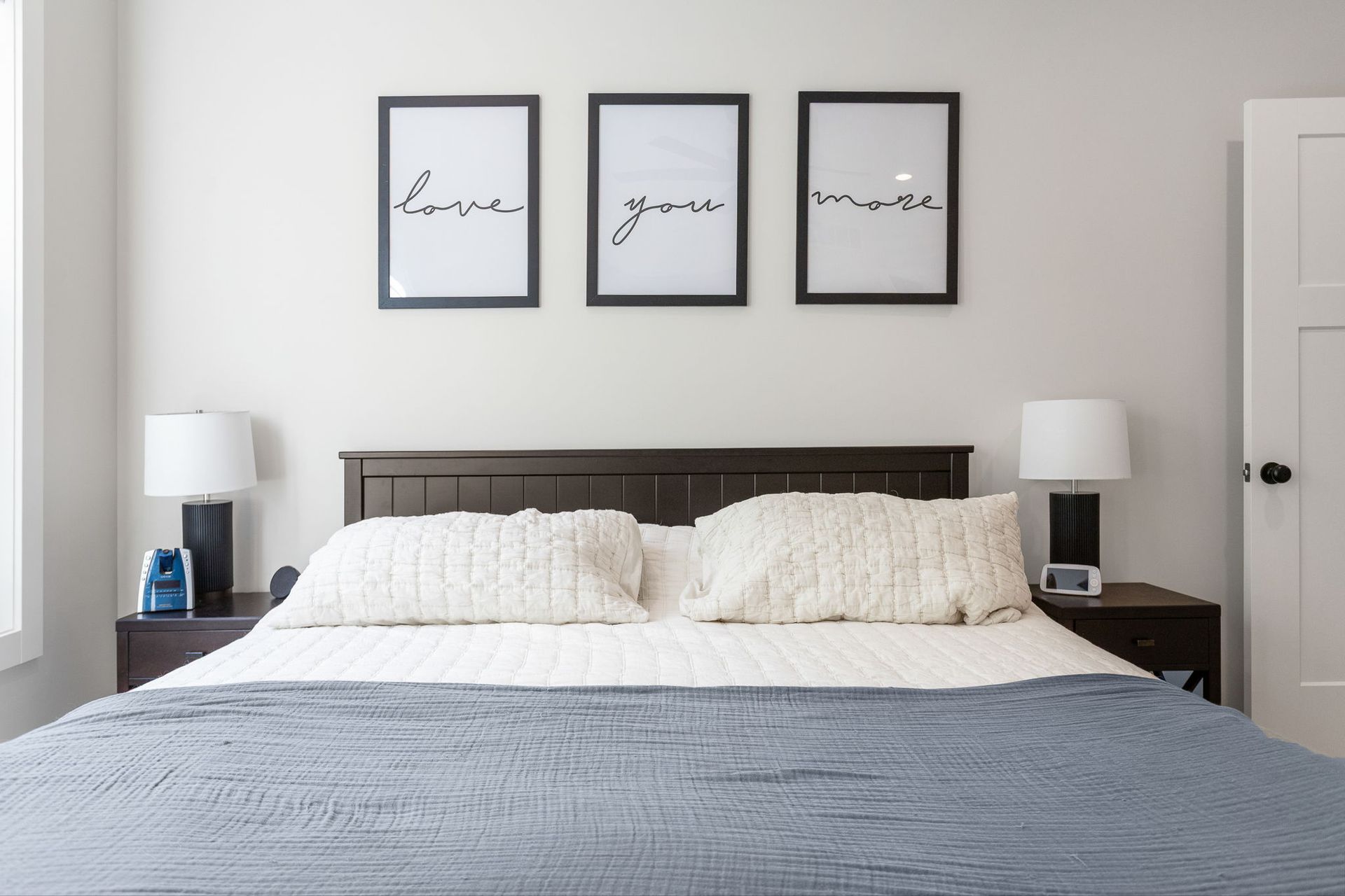 A bed with a dark headboard, white pillows, a blue blanket, and three framed signs reading 